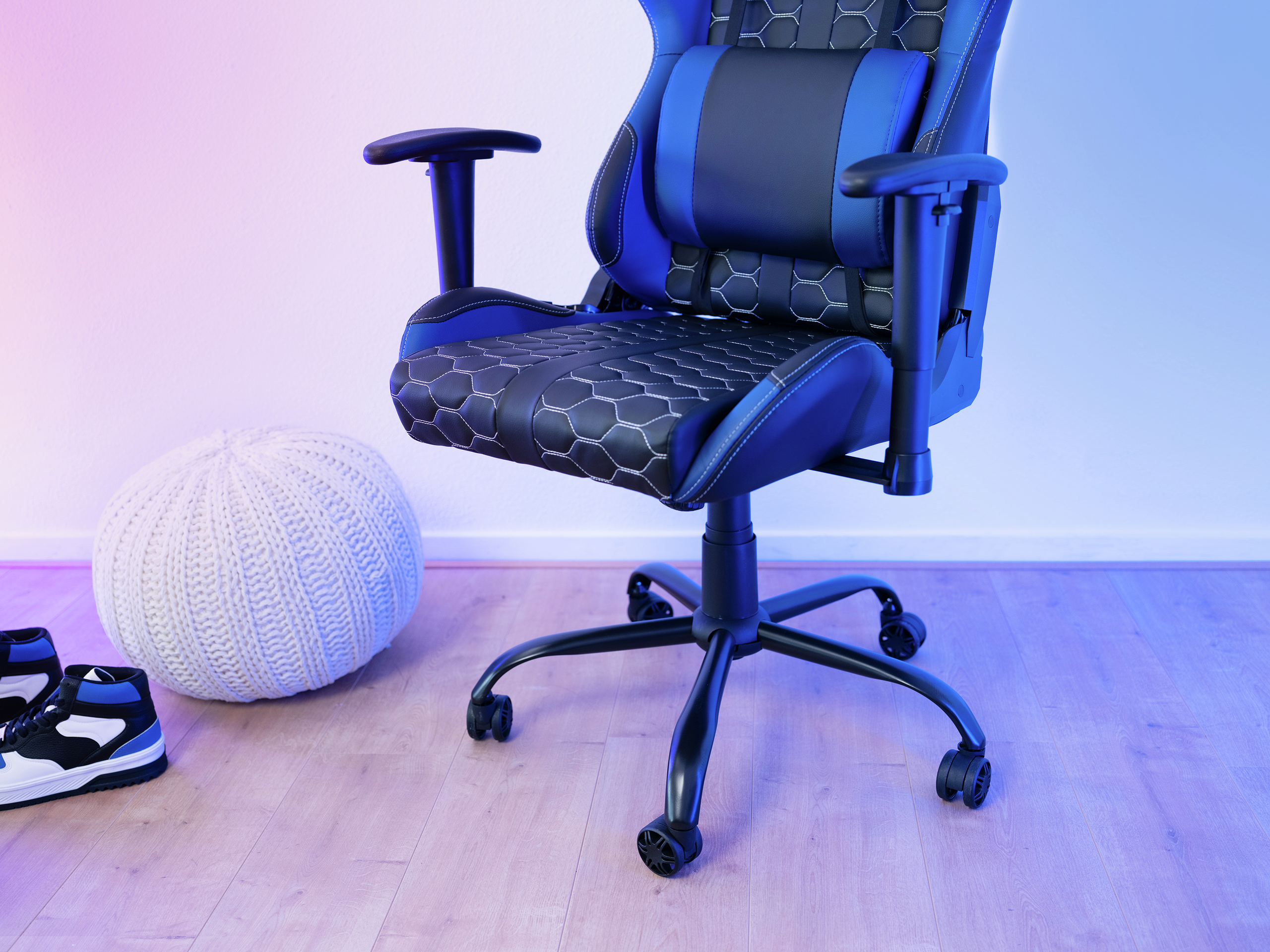 Krzesło do gier z czarną podstawą, niebieskimi i czarnymi akcentami i białymi szwami. Biała pufa i buty.