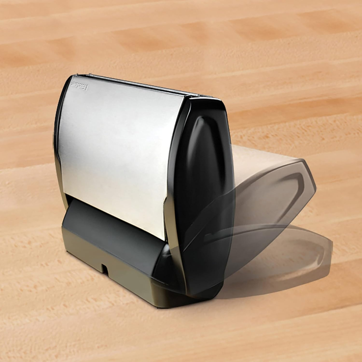 Un dispenser di carta assorbente nero e argento, parzialmente aperto, posto su una superficie di legno.