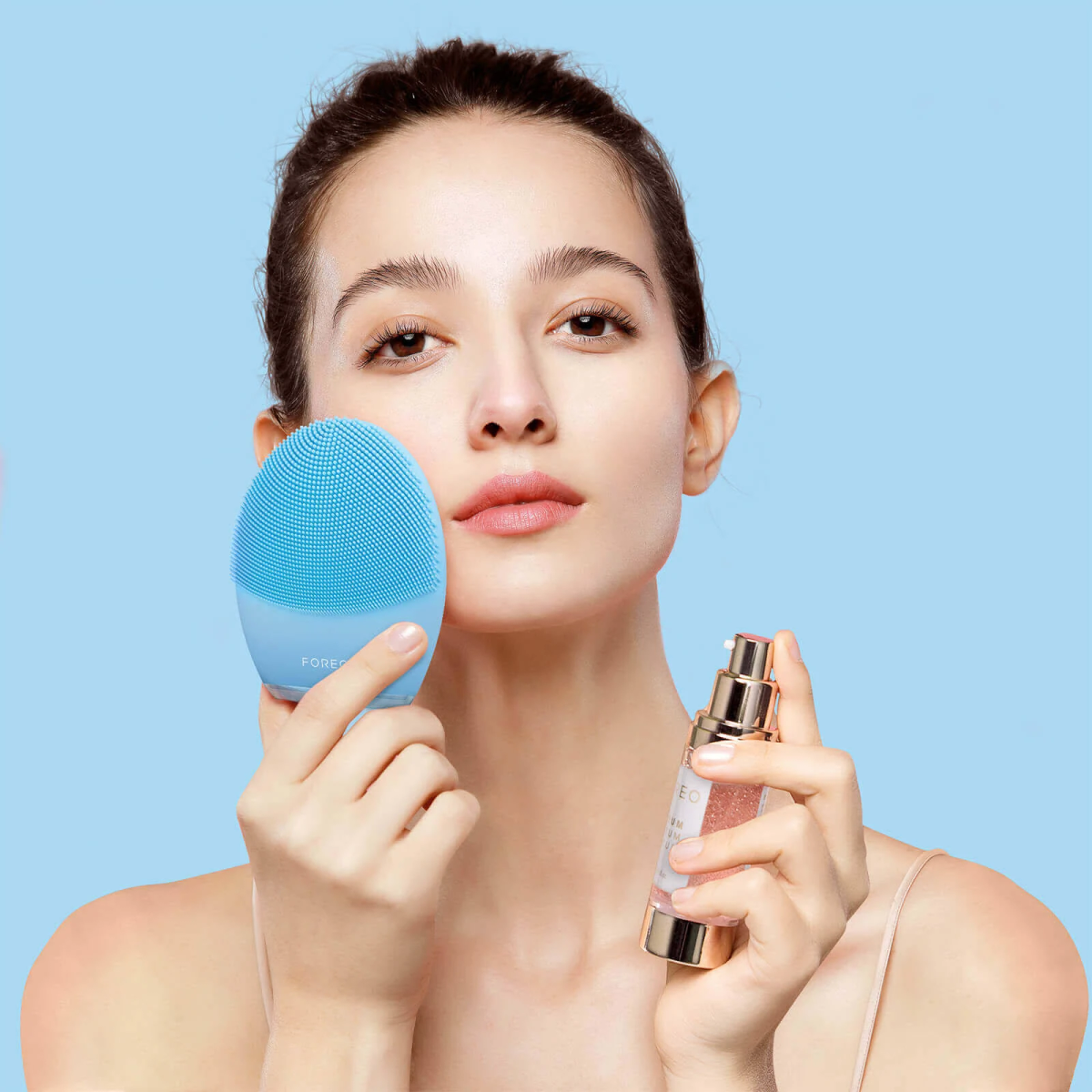 Mujer sosteniendo un cepillo facial azul y producto para el cuidado de la piel, sobre fondo azul.