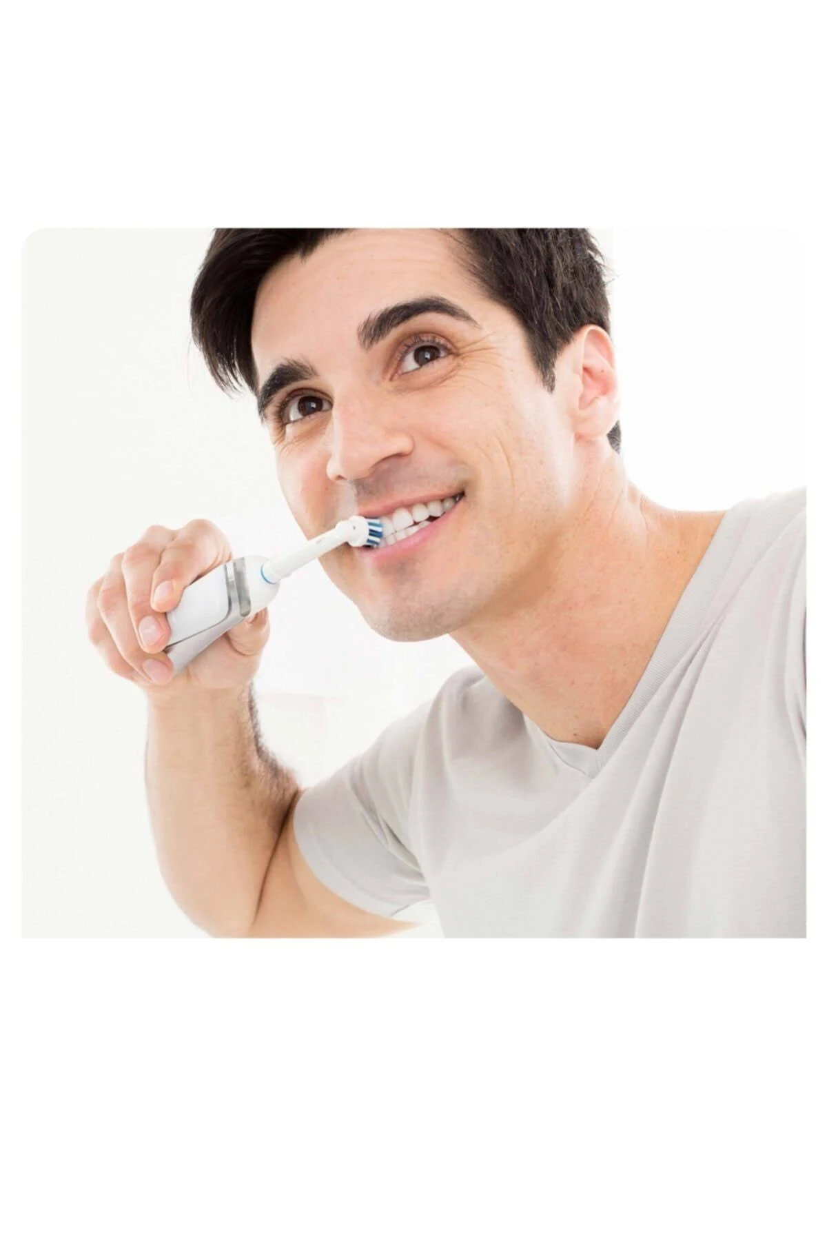 Hombre cepillándose los dientes con cepillo eléctrico. Sonríe y mira hacia arriba.