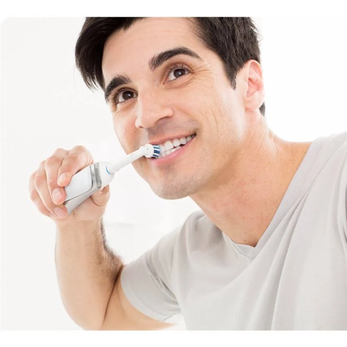 Man brushing his teeth with an electric toothbrush. He is smiling and has short dark hair.