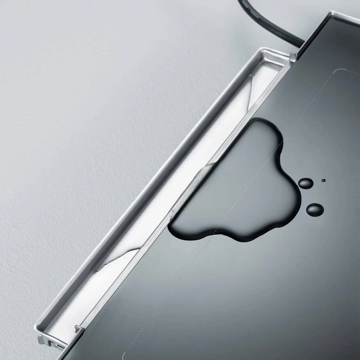 Bandeja de acero inoxidable con agua derramada y gotas sobre fondo gris.