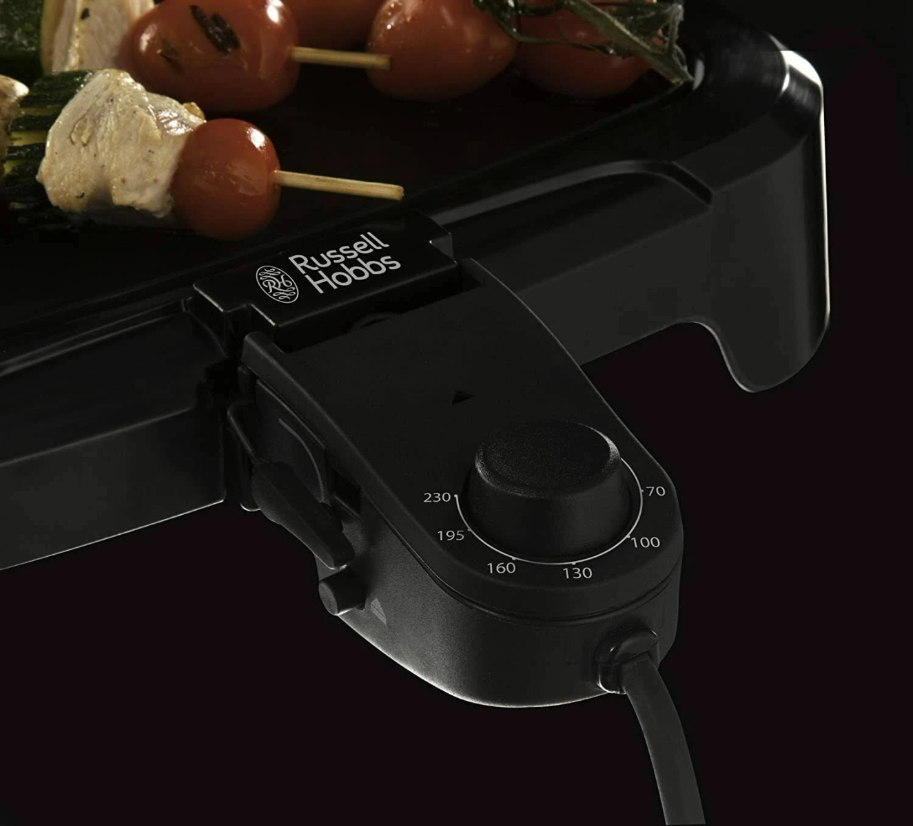 Nahaufnahme eines schwarzen Russell Hobbs Grills mit Temperaturregler. Aufgespießte Tomaten und Hähnchen oben.