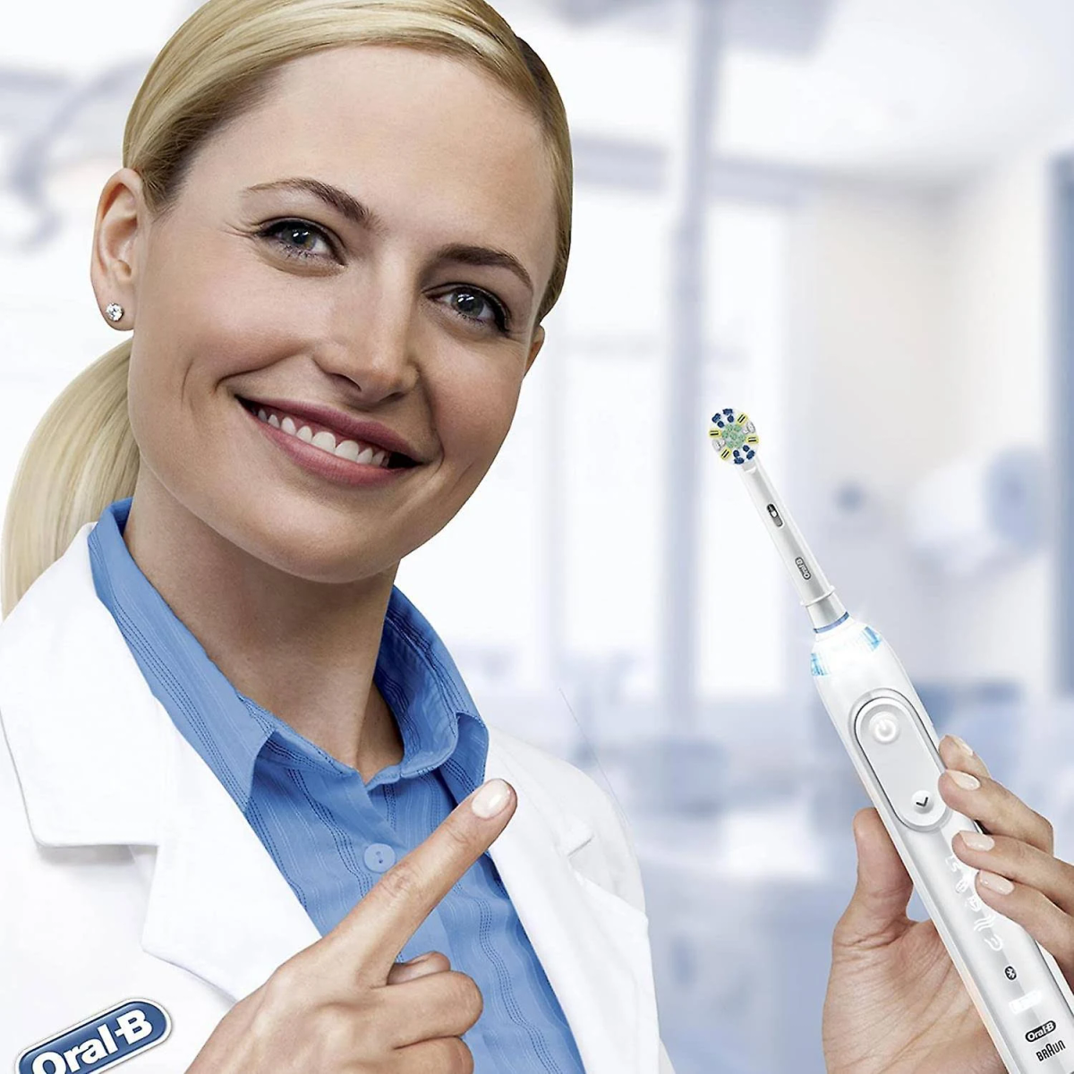 Donna bionda in camice da laboratorio che indica uno spazzolino elettrico. Logo Oral-B visibile.