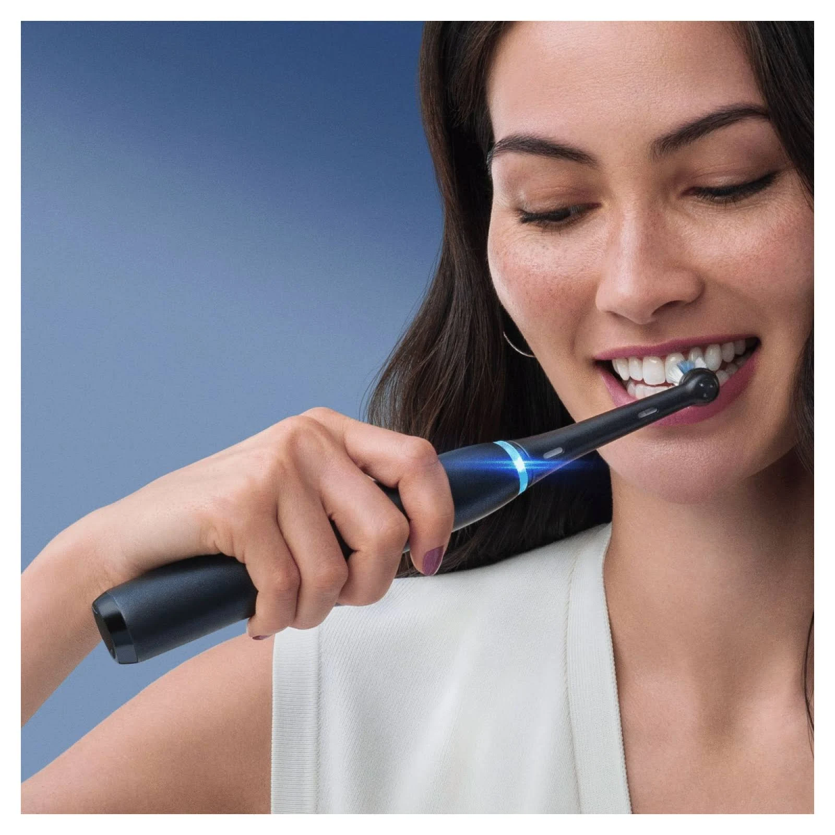 Mujer cepillándose los dientes con cepillo eléctrico negro, sonriendo.