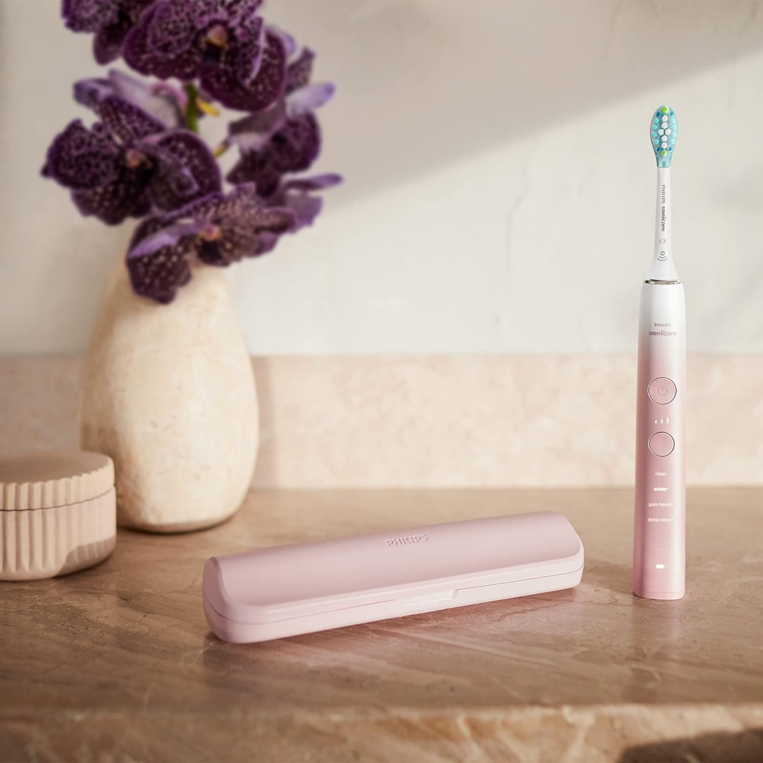 Spazzolino rosa con custodia rosa e fiori. Superficie bianca pulita con vaso sullo sfondo.