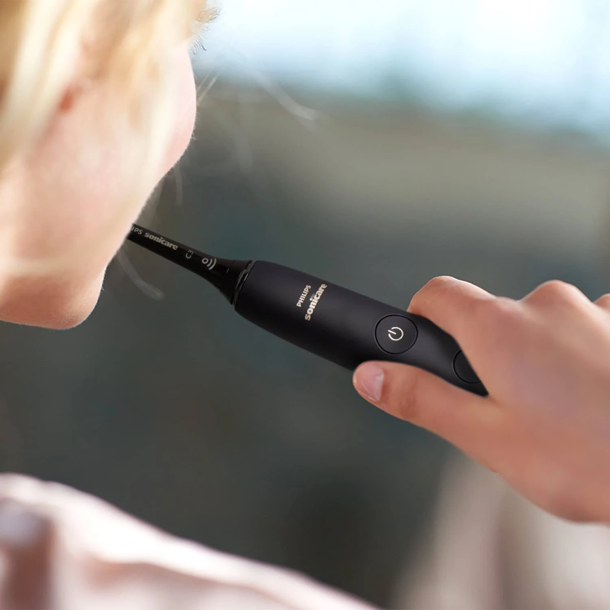 Osoba trzymająca czarną elektryczną szczoteczkę do zębów, myjąca zęby. Widoczna nazwa marki.