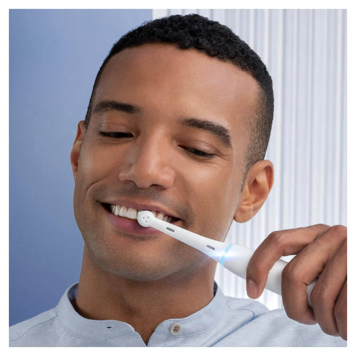 Uomo che si lava i denti con uno spazzolino elettrico bianco, sorridente, su sfondo blu.