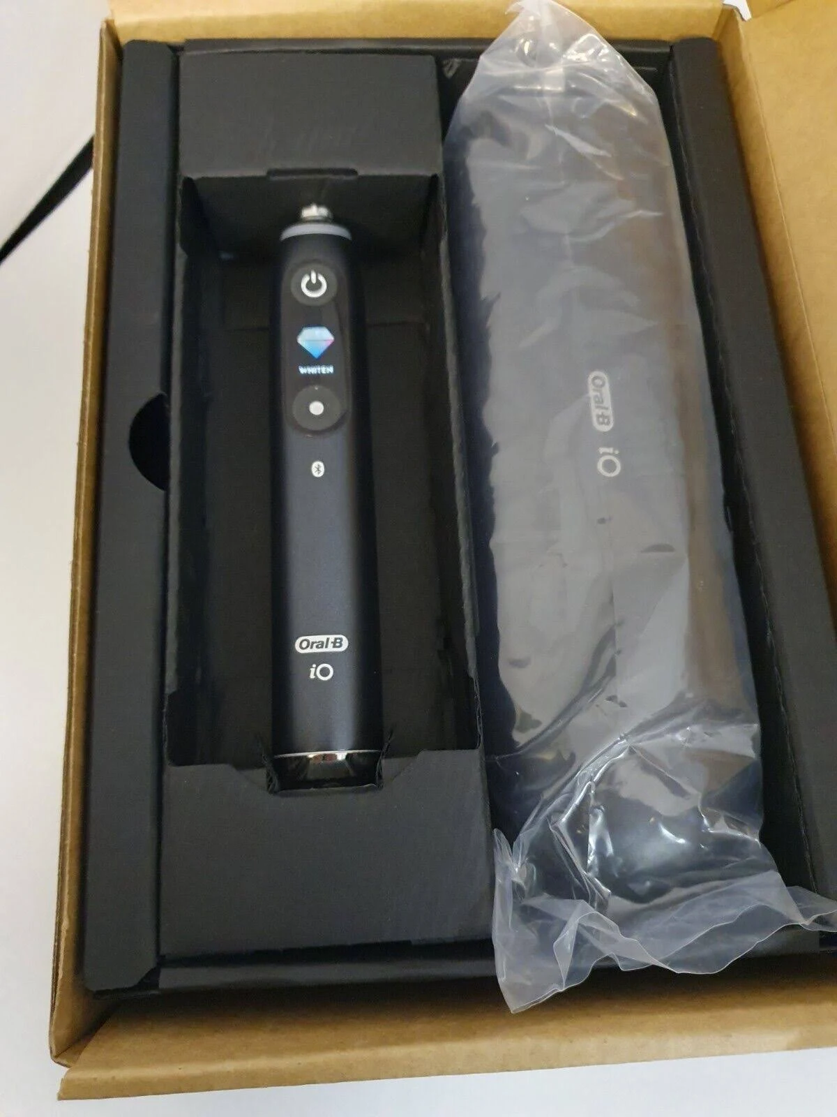 Schwarze elektrische Zahnbürste Oral-B iO und Ladegerät in einer geöffneten schwarzen Box auf einer Oberfläche.
