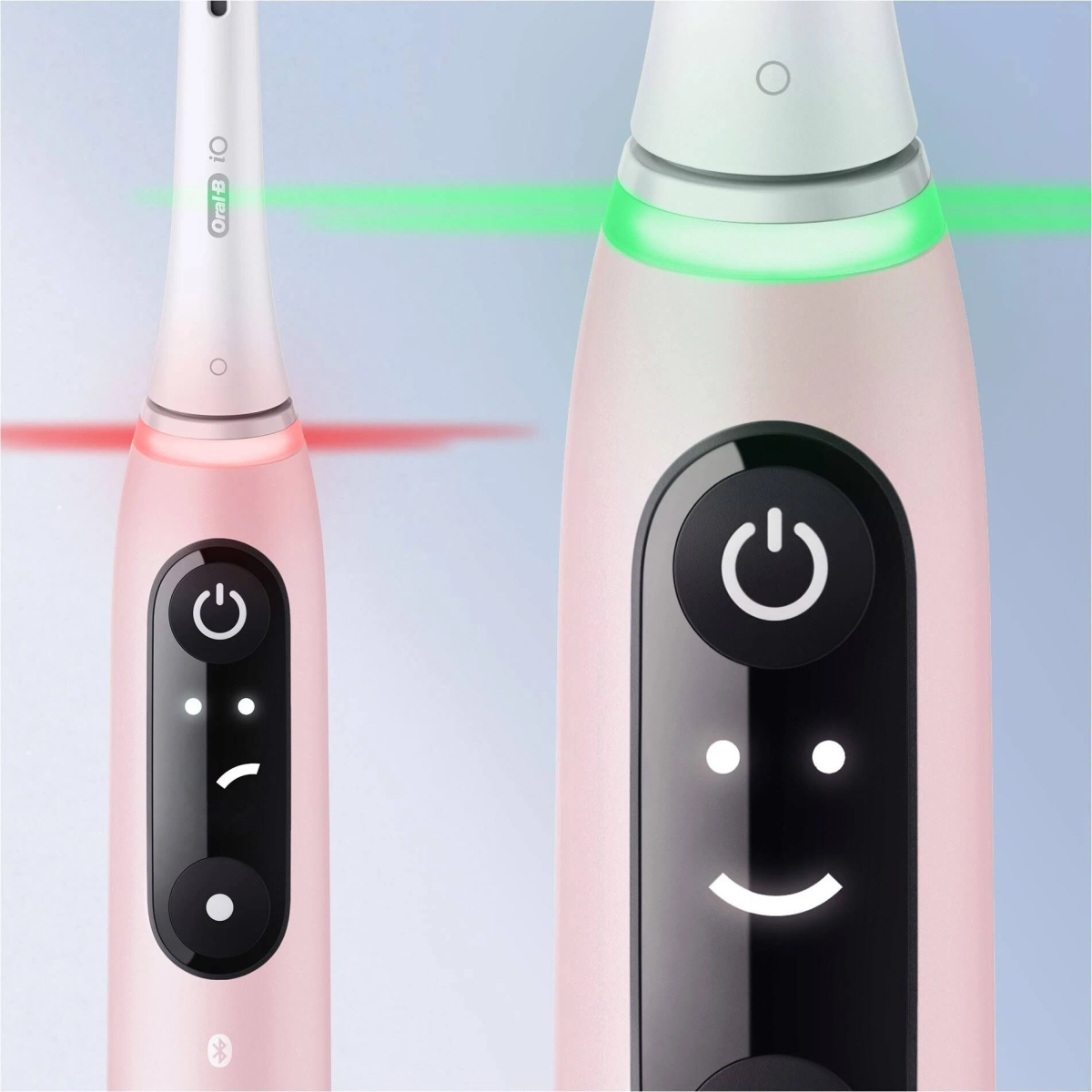 Close-up of two pink electric toothbrushes. One shows a smiling face on the power button. The other has a light.