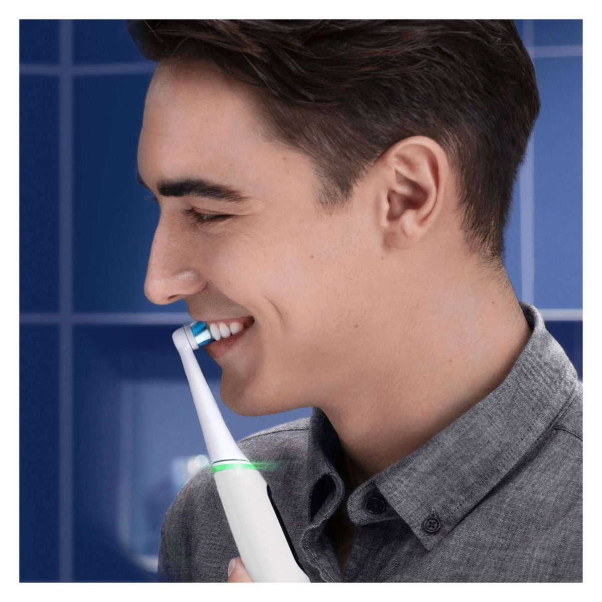 A man smiling while brushing his teeth with an electric toothbrush.