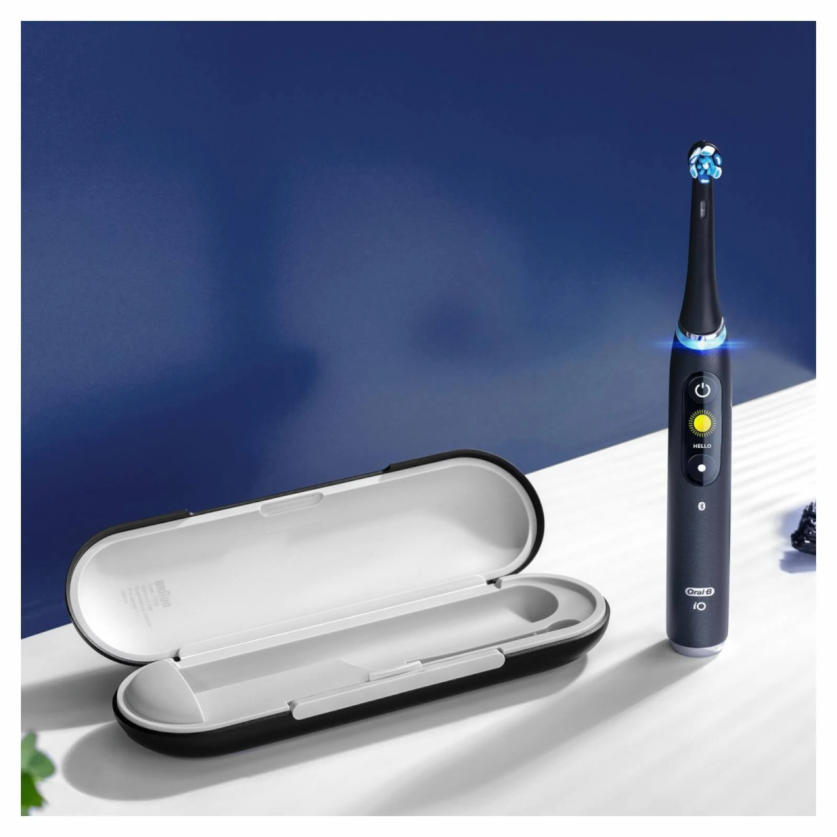 Cepillo dental eléctrico negro y estuche abierto sobre superficie blanca con fondo azul.