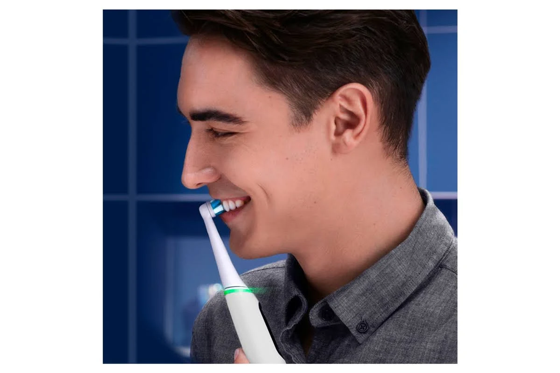 Un uomo si lava i denti con uno spazzolino elettrico, sorridendo leggermente.