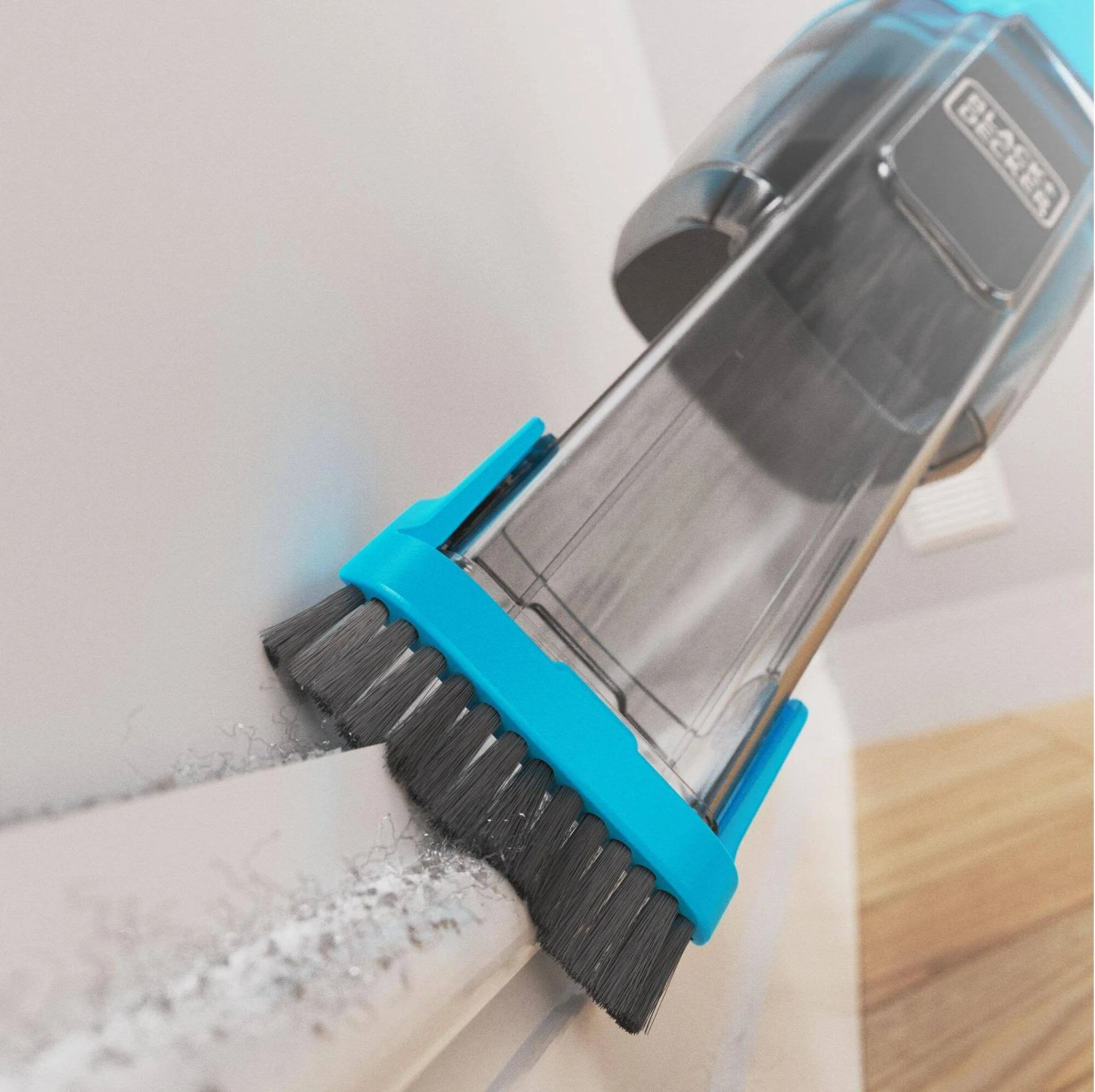 Una aspiradora de mano Black + Decker limpiando una superficie blanca. El cepillo es azul.