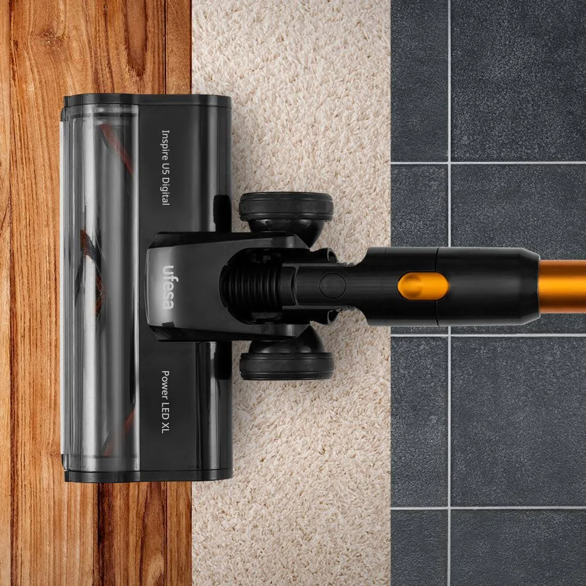 Testa dell'aspirapolvere su pavimento in legno e zona moquette. Colori nero e arancione.