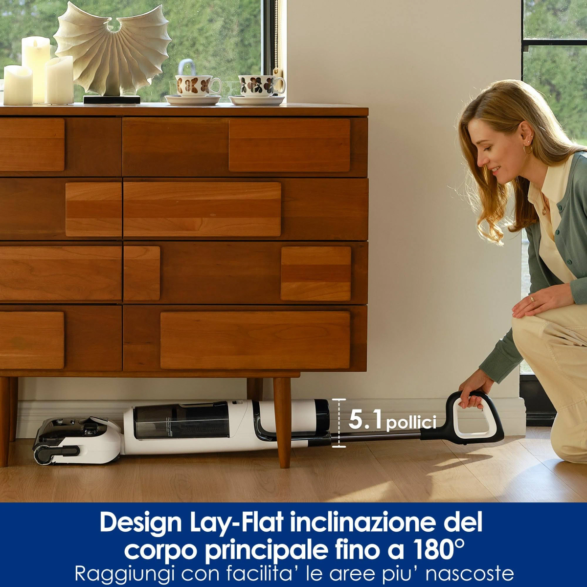 Una mujer usando una aspiradora debajo de un mueble de madera. La aspiradora es plana, alcanzando debajo del mueble.