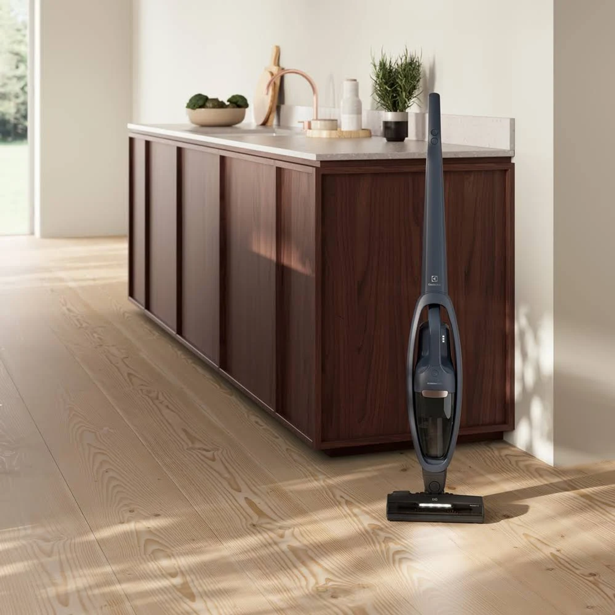 Un aspirapolvere senza fili Electrolux blu scuro in piedi su un pavimento in legno, vicino a mobili.