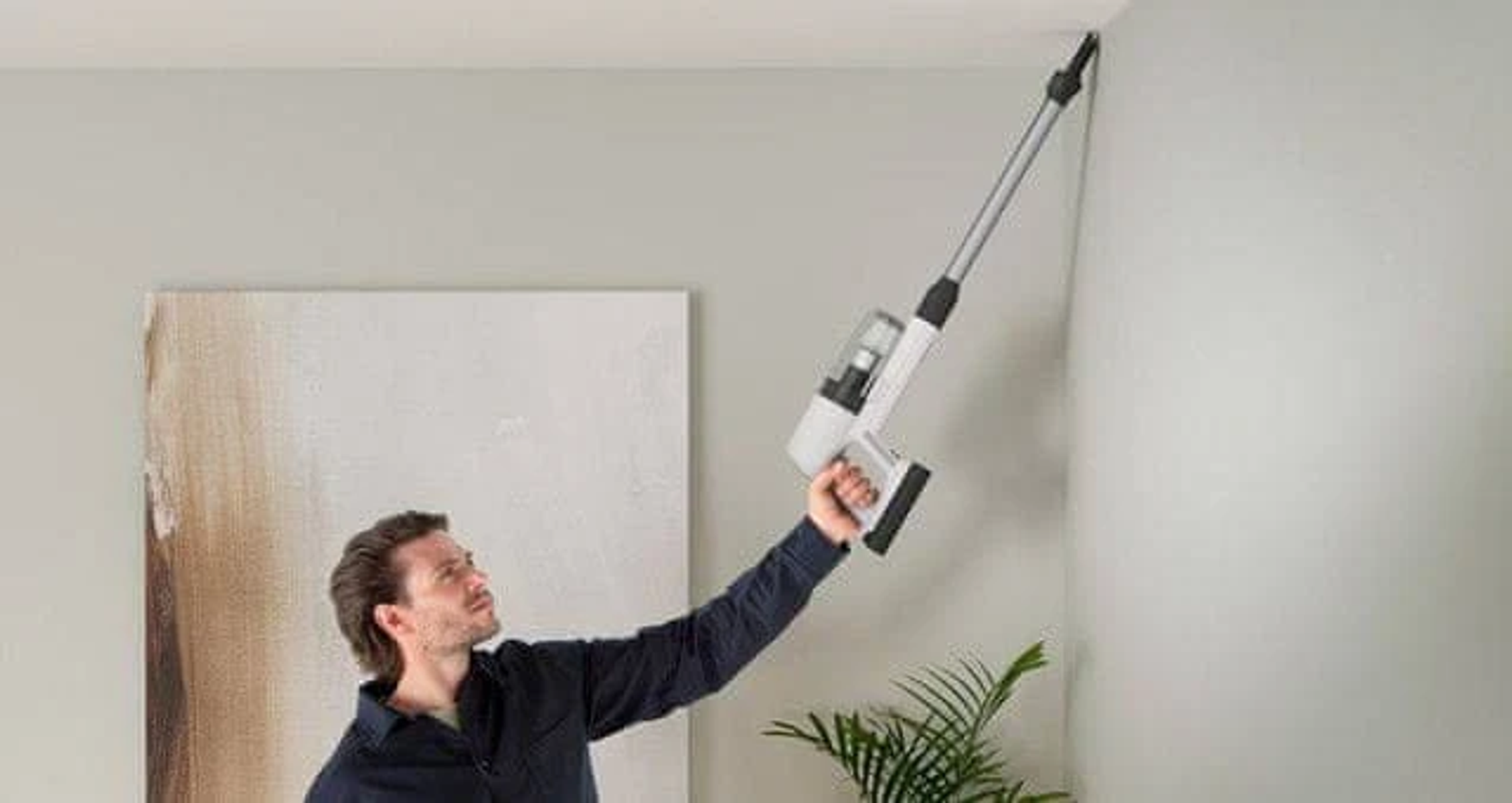 Un hombre está aspirando la esquina de una habitación con una aspiradora inalámbrica.