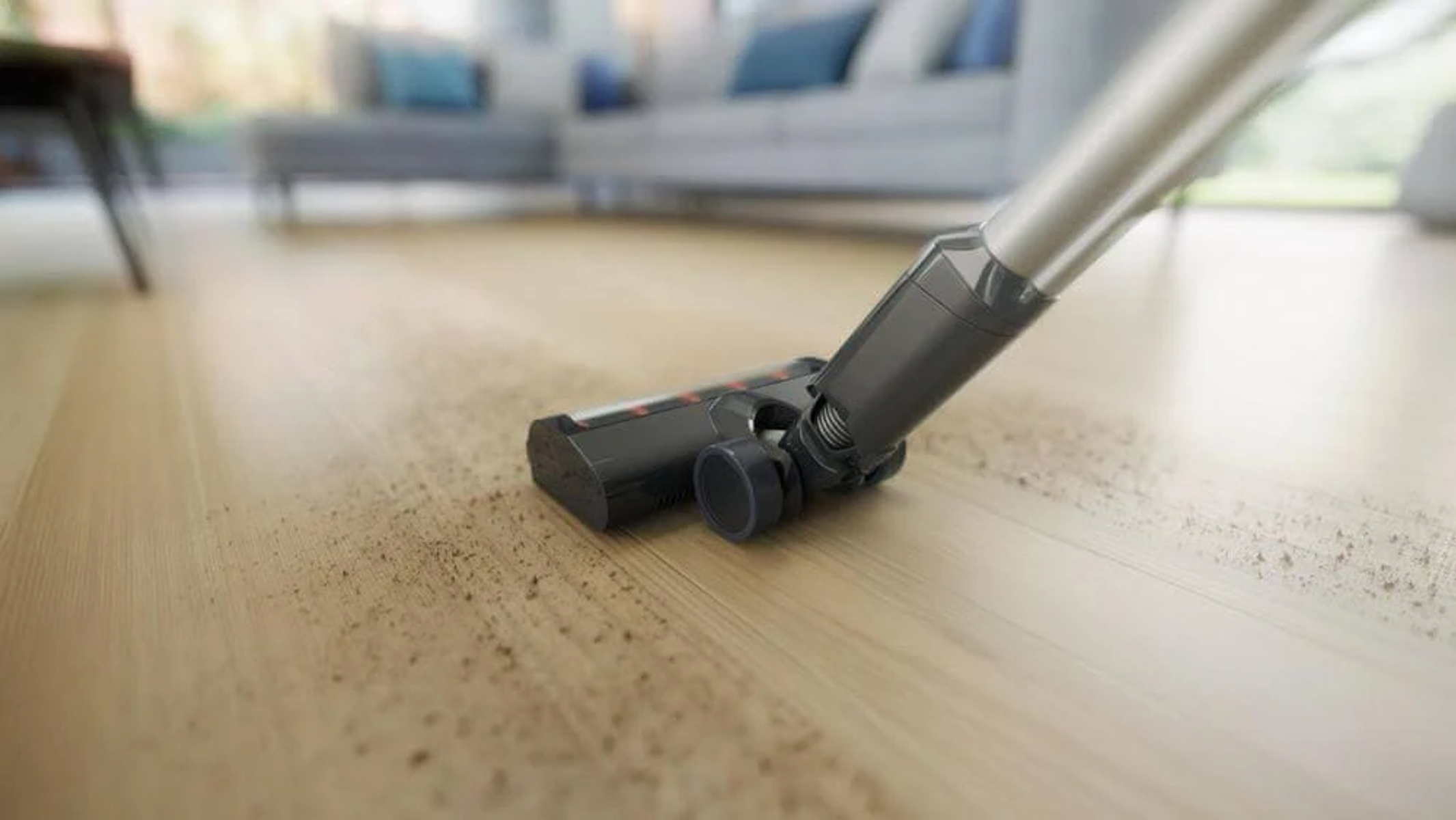 Primo piano di una testina dell'aspirapolvere che pulisce un pavimento in legno. Detriti visibili.