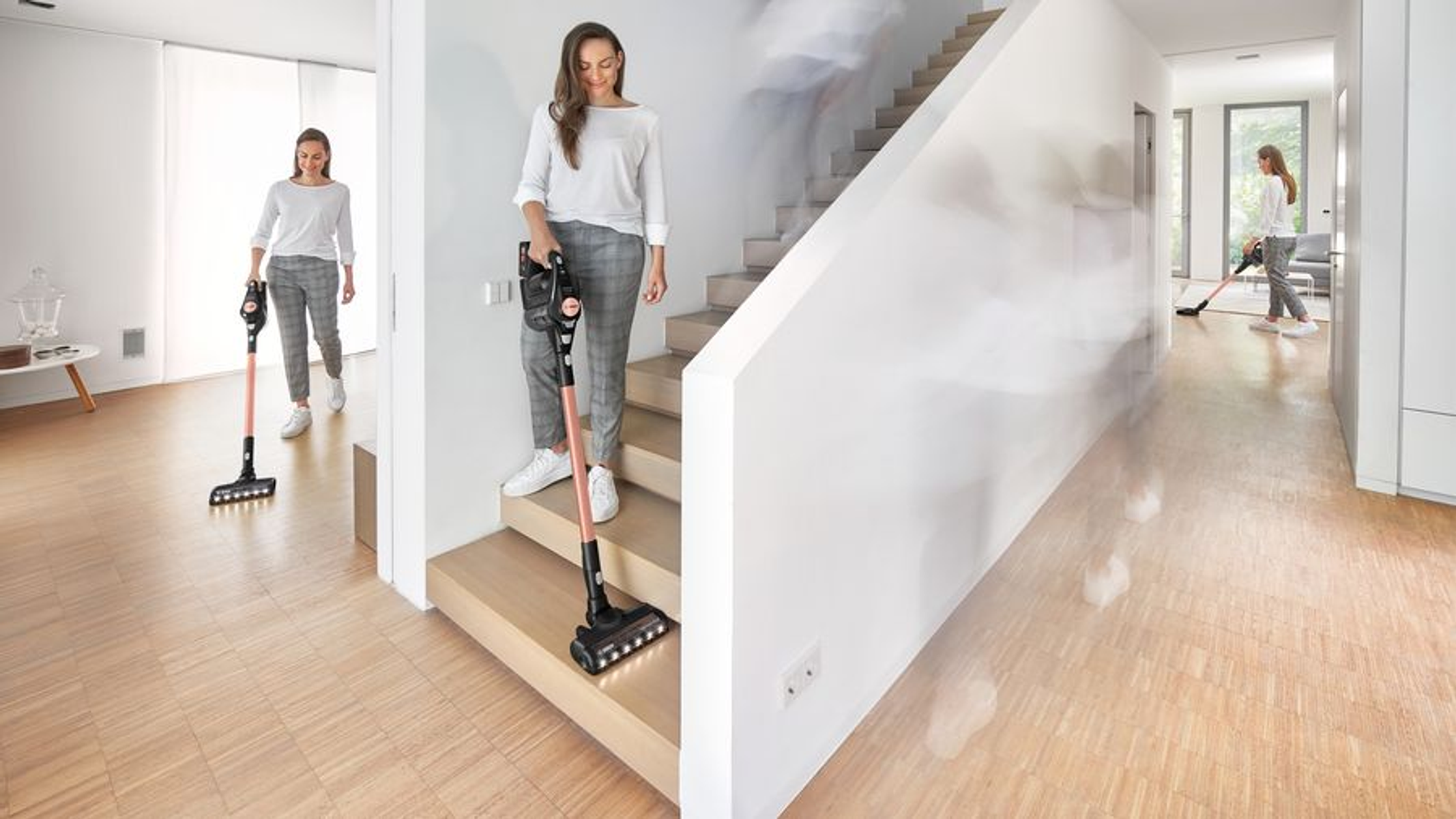 Kobieta odkurza schody, inna korytarz. Trzecia osoba odkurza dalej. Drewniane podłogi.