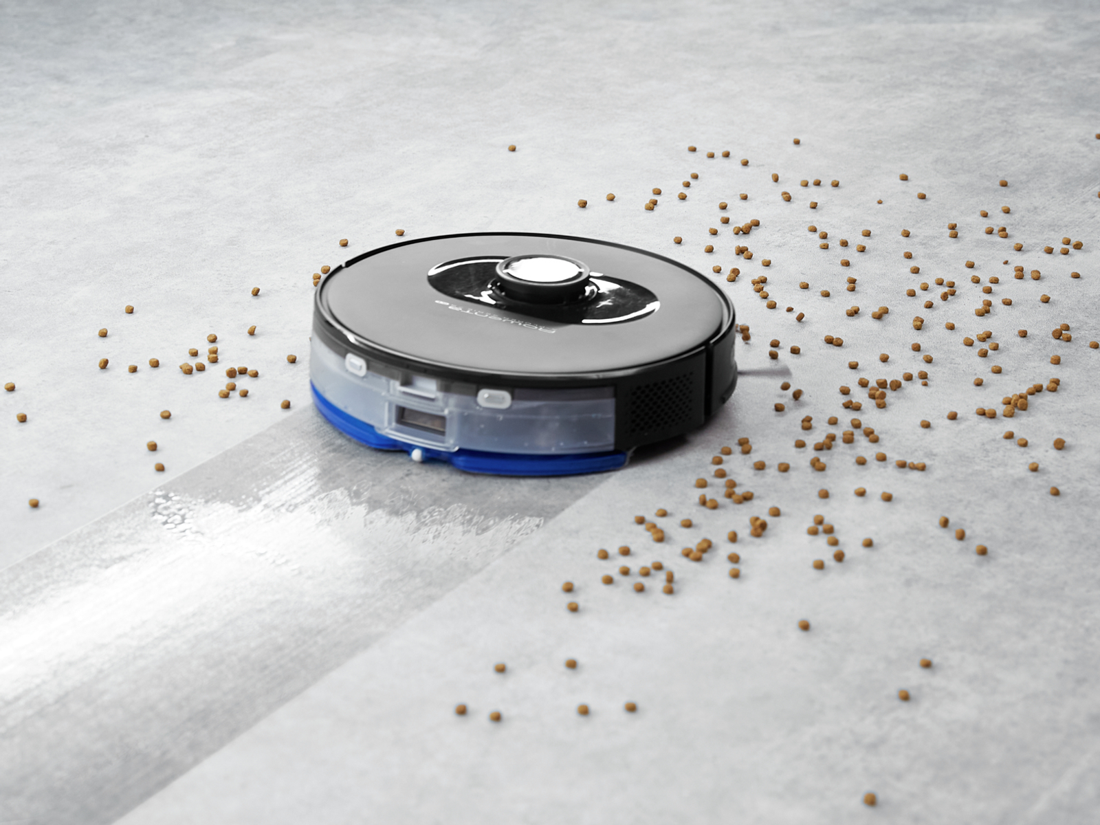Aspirapolvere robot che pulisce un pavimento. Pellet marroni sparsi sul pavimento. Sfondo grigio.