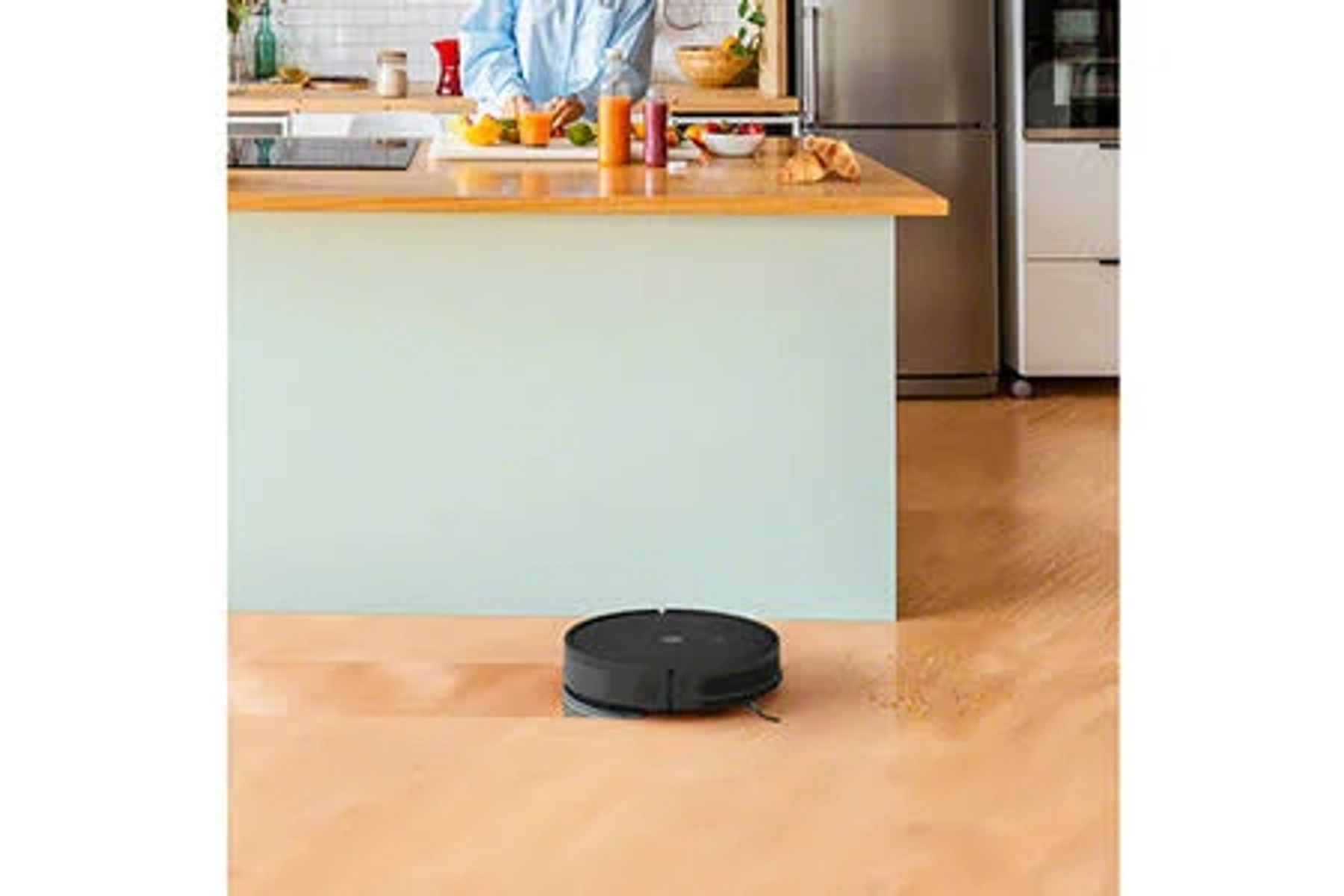Robot aspirapolvere su un pavimento, sfondo mostra una cucina con una persona.