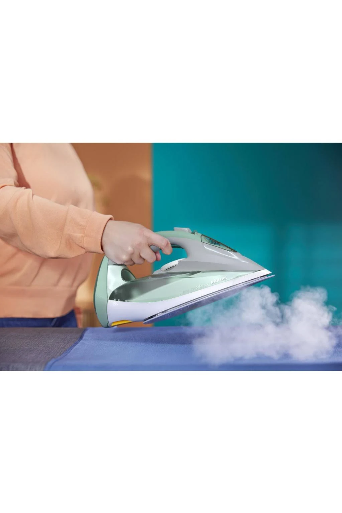 Osoba prasuje na niebieskiej powierzchni. Widoczna para, żelazko zielono-białe.