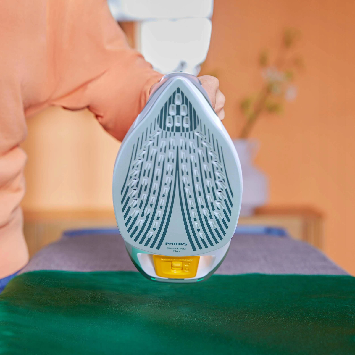 Osoba trzyma biało-szare żelazko parowe Philips nad zieloną deską do prasowania.