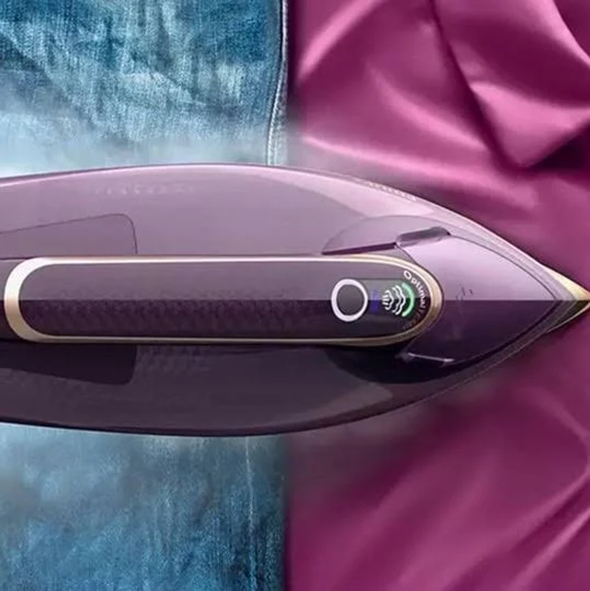 Żelazko parowe, w połowie na fioletowej tkaninie, w połowie na niebieskim dżinsie. Nowoczesny design.