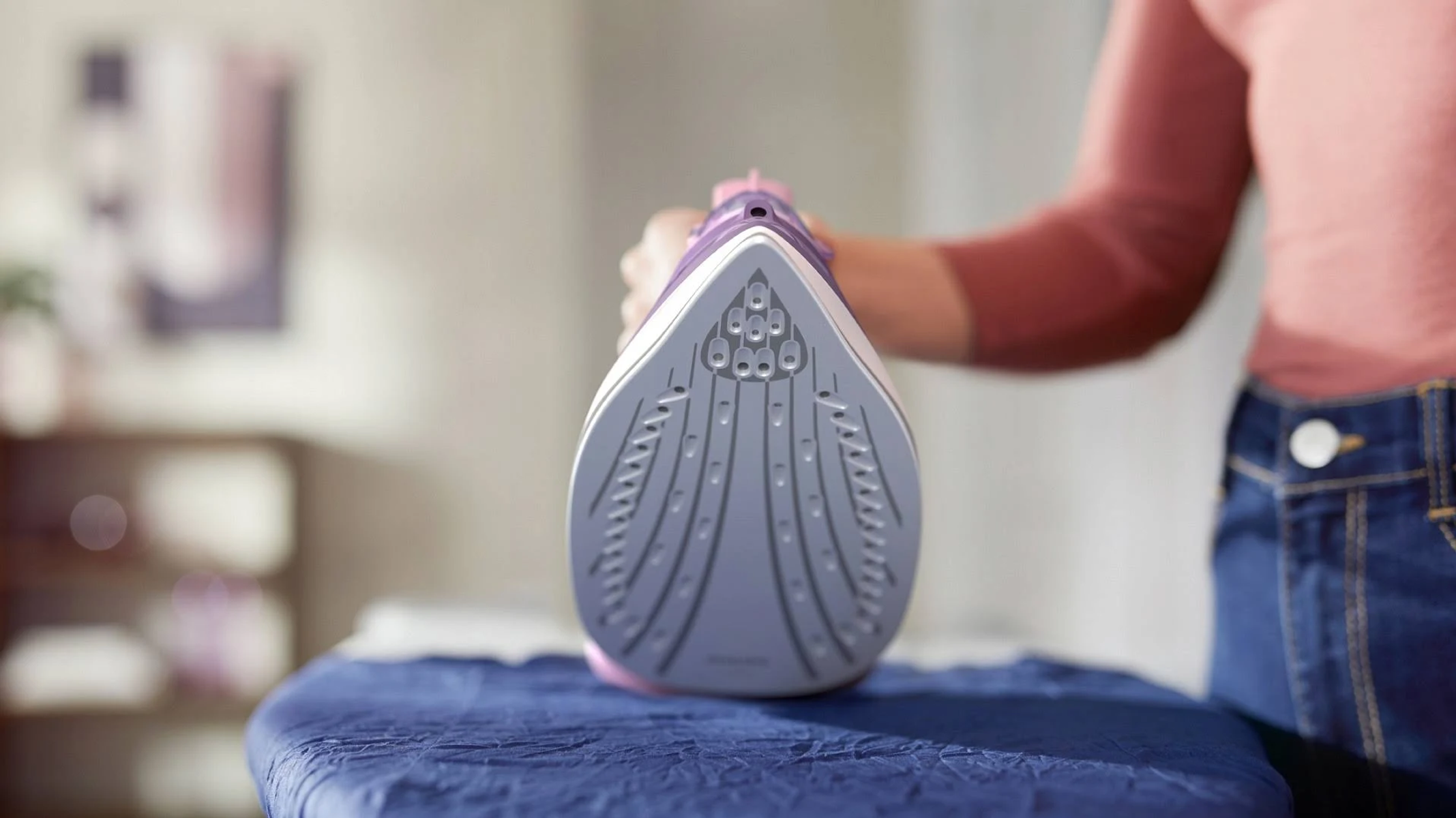 Osoba trzymająca żelazko nad deską do prasowania. Widoczna stopa żelazka.