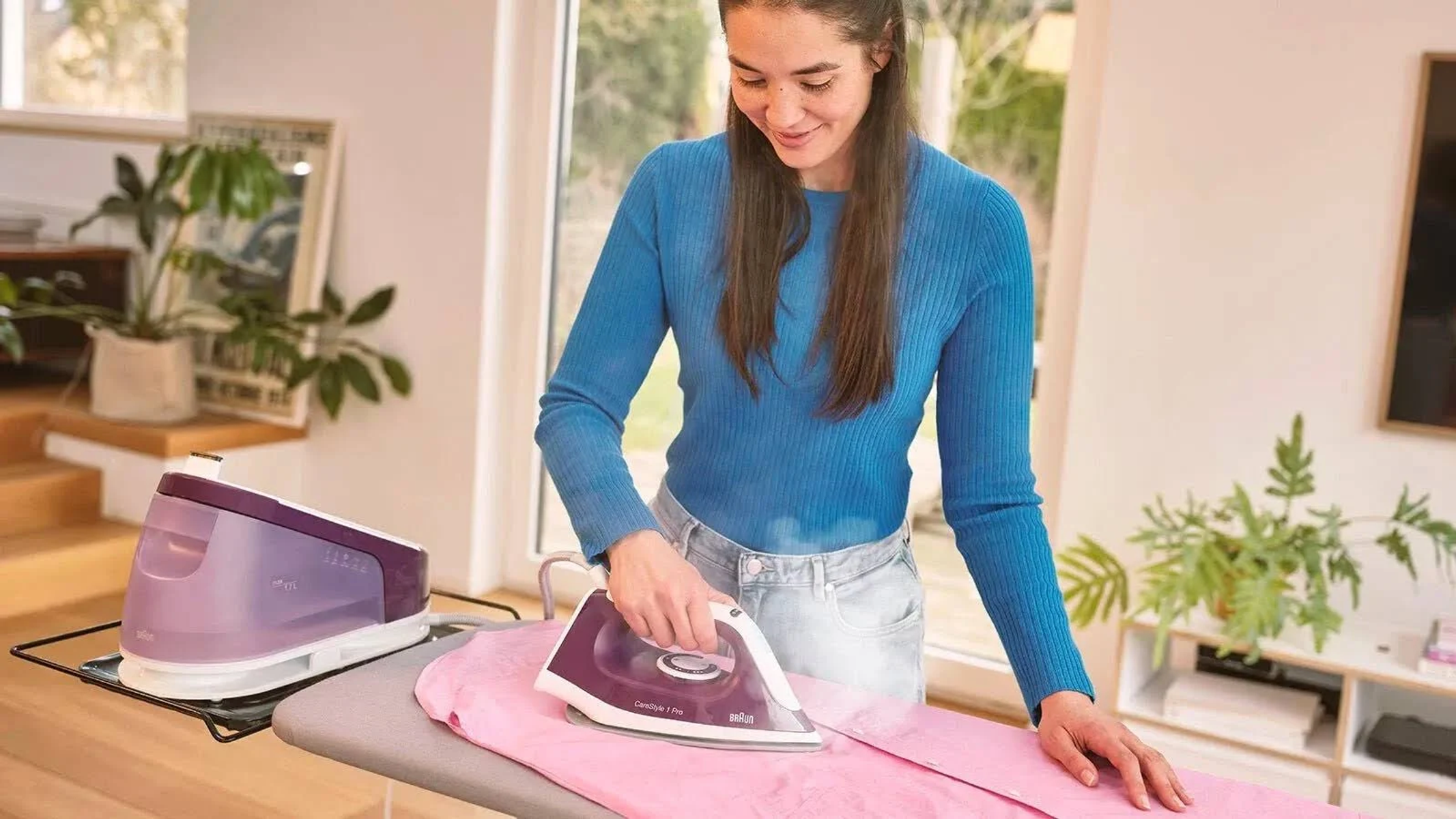 Frau bügelt rosa Stoff mit einem lila Dampfbügeleisen auf einem Bügelbrett.