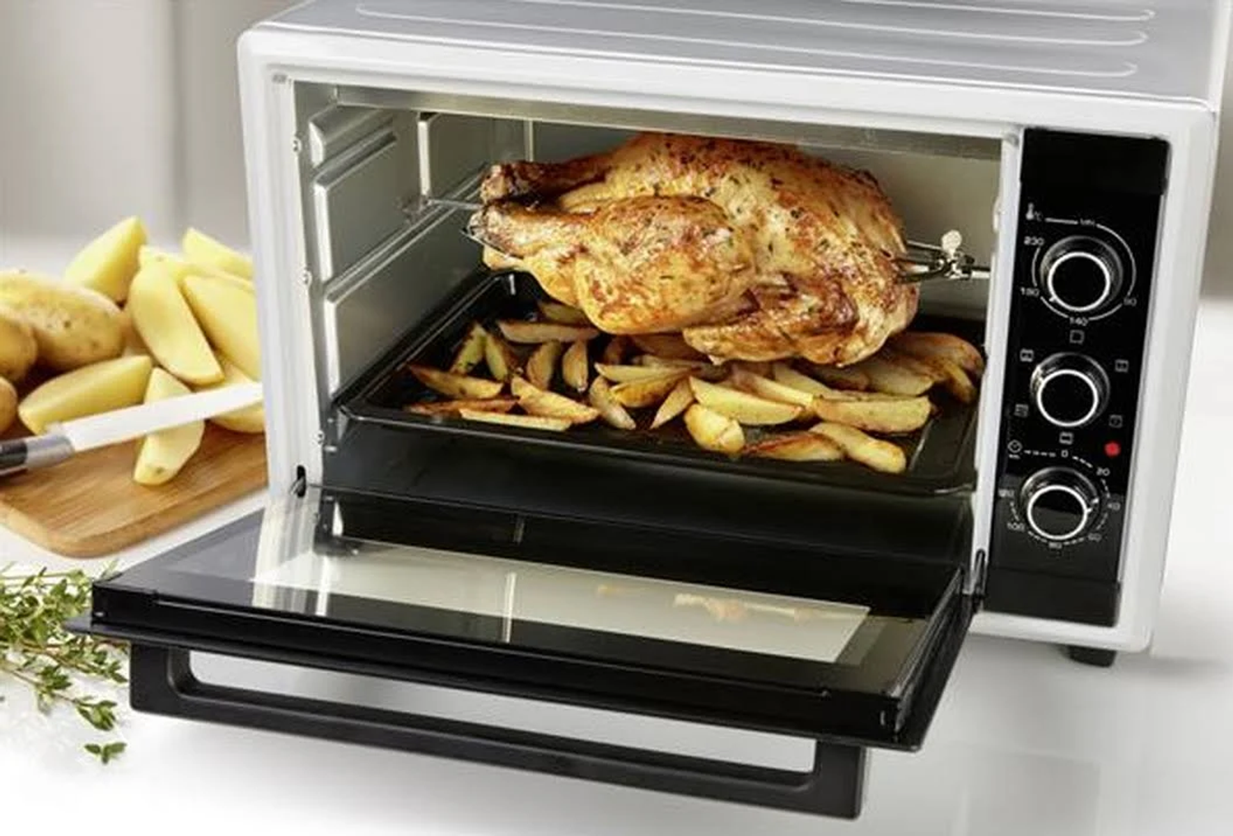 Piekarnik z otwartymi drzwiami, pieczony kurczak i frytki na czarnej tacy.