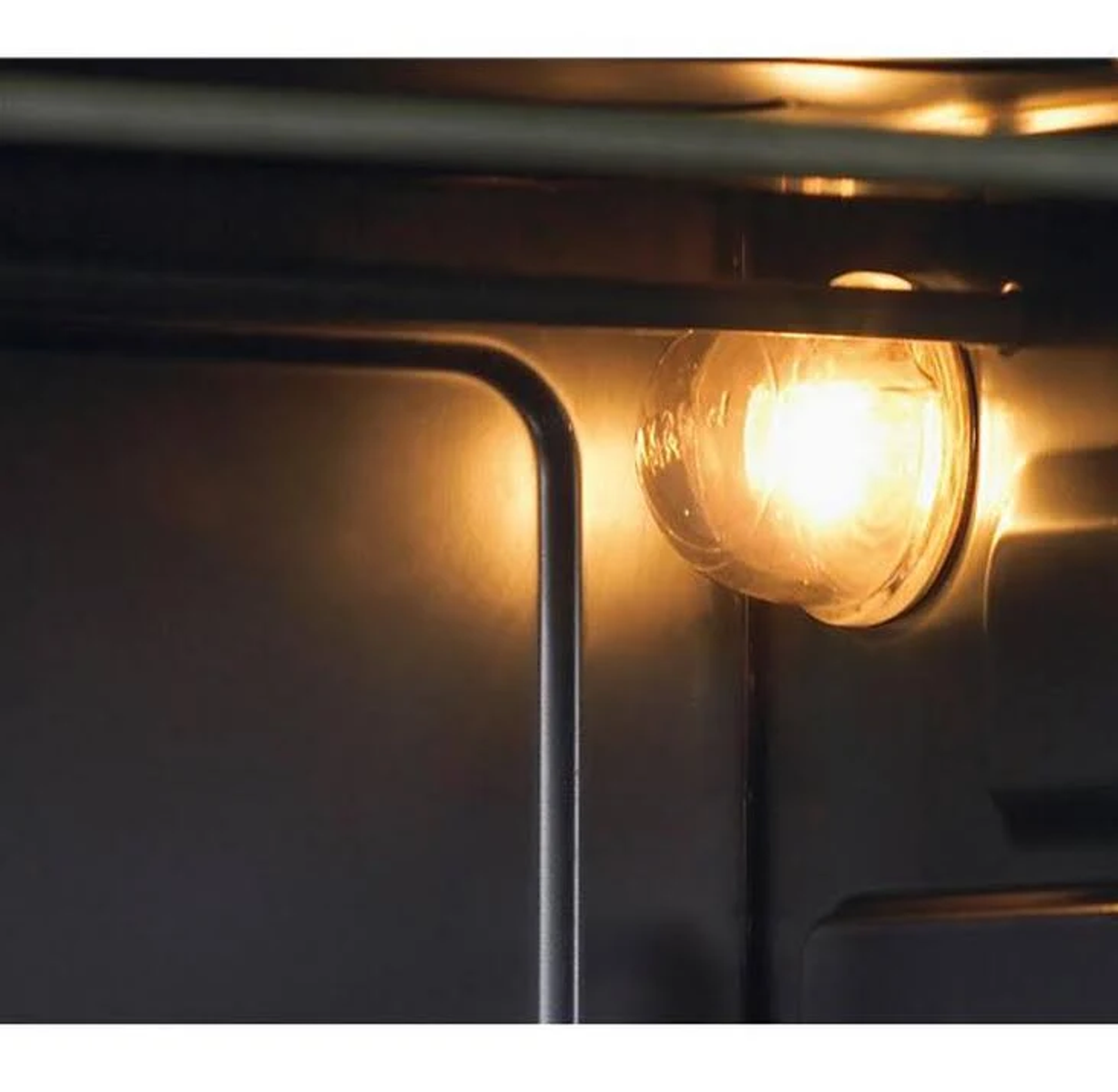 Zbliżenie wnętrza piekarnika, pokazujące zapaloną żarówkę. Ciemne wnętrze.