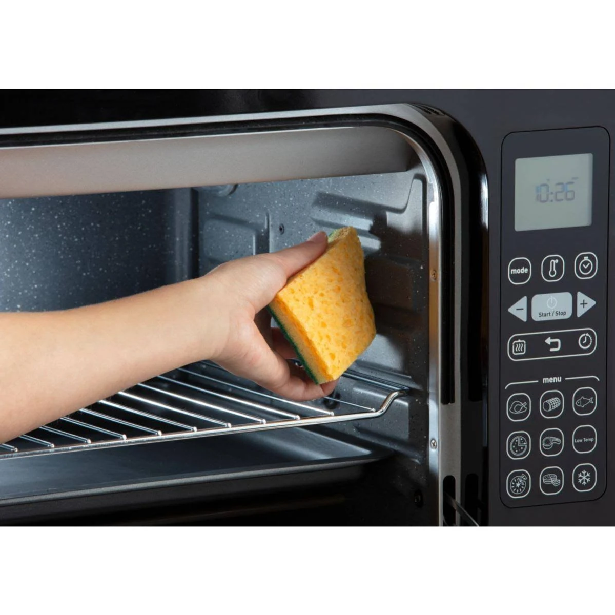 Mano con spugna dentro un forno nero. La spugna è gialla e verde, pulisce la griglia.