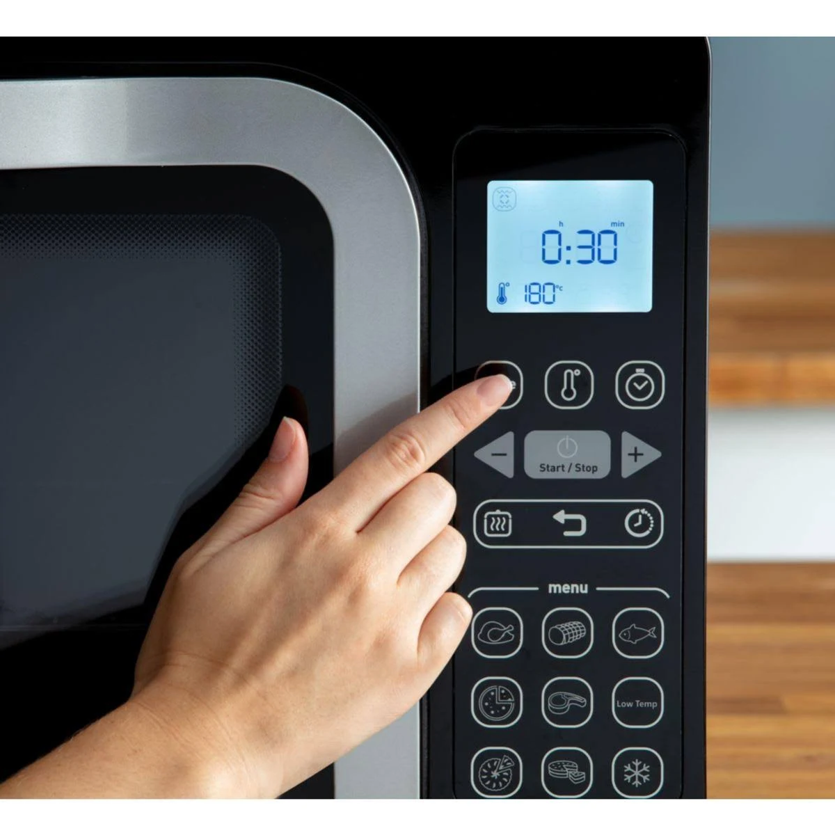 Mano che preme un pulsante su un microonde. Il display mostra timer, temperatura e impostazioni.