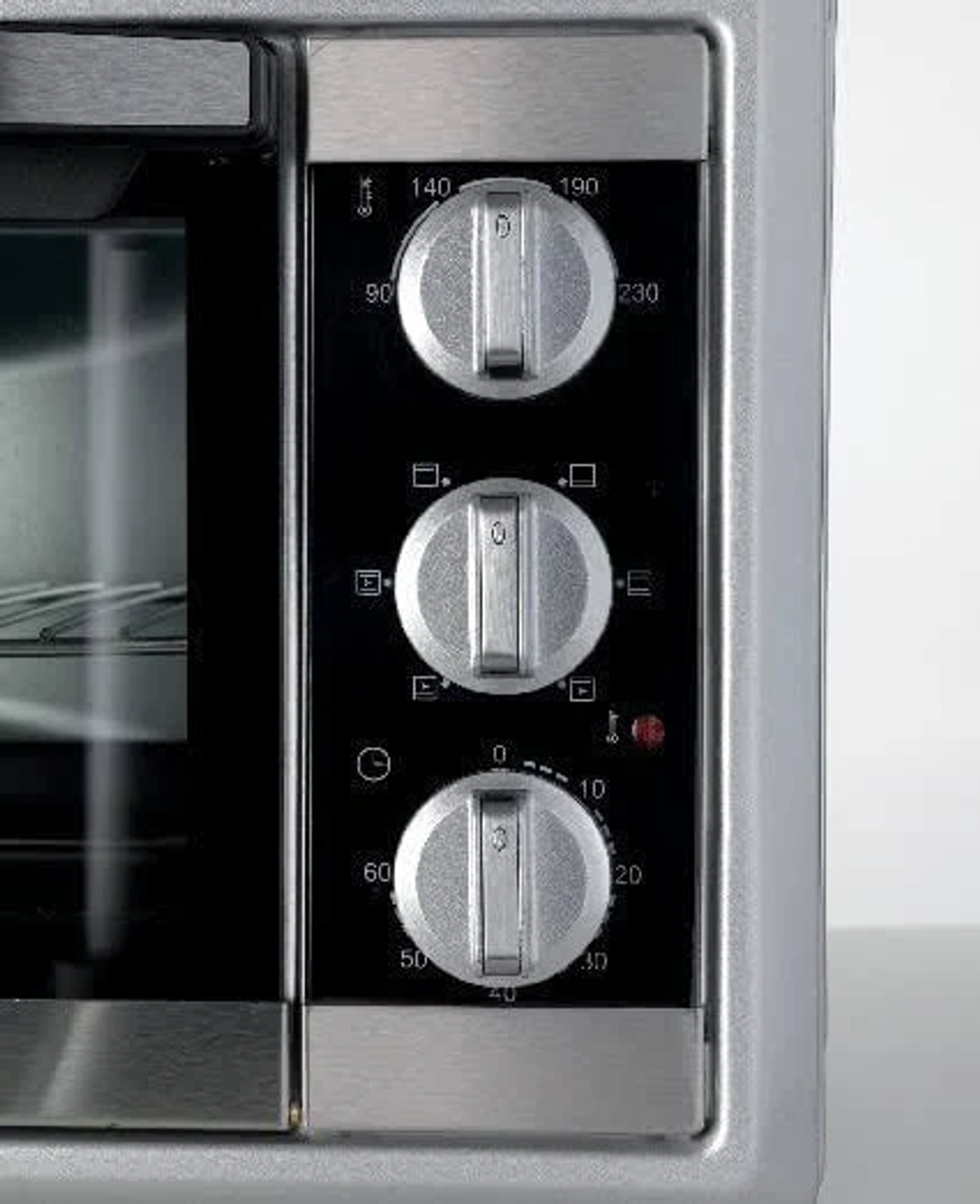 Primer plano del panel de control del horno. Muestra diales de temperatura, tiempo y función. Acabado plateado.