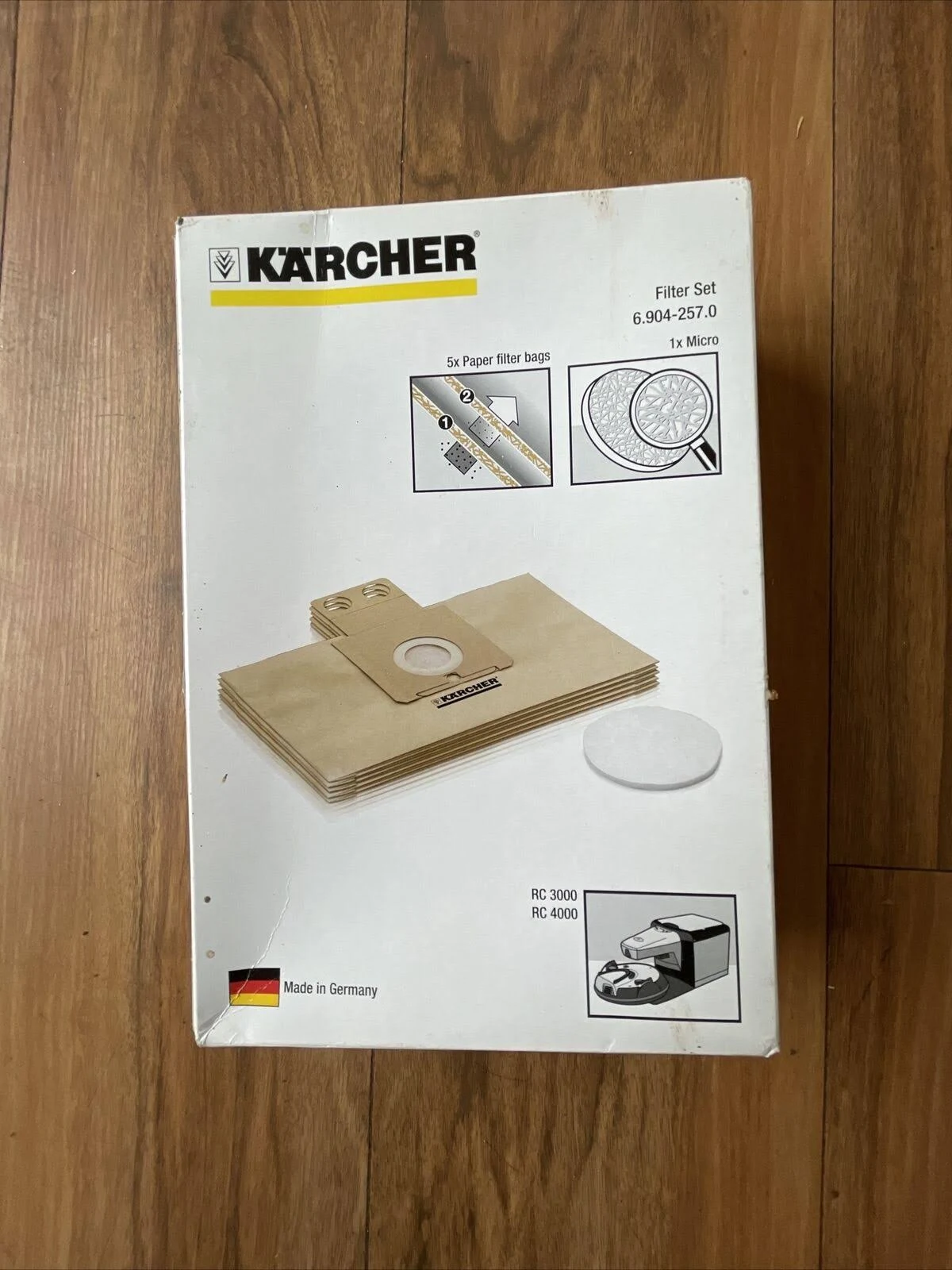 Scatola del set di filtri per aspirapolvere Kärcher su pavimento in legno. La scatola è bianca con immagini e testo.