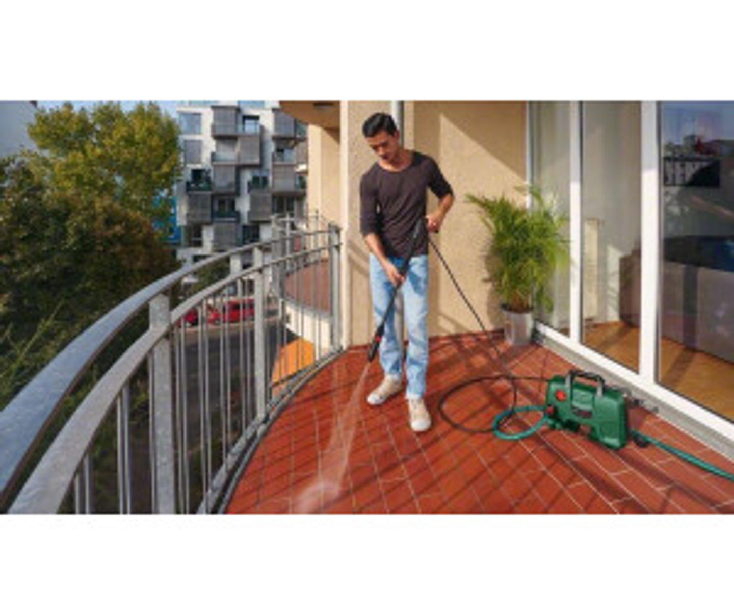 Un homme utilise un nettoyeur haute pression sur un balcon avec un sol en briques.