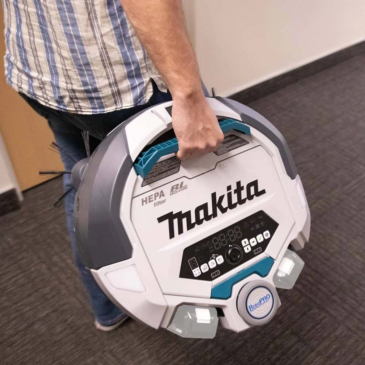 Aspirapolvere robot tenuto da una persona. L'aspirapolvere è bianco e grigio, marchio Makita.
