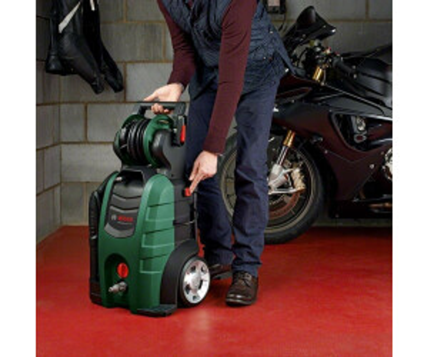 Un uomo vicino a una idropulitrice verde e una moto in un garage.
