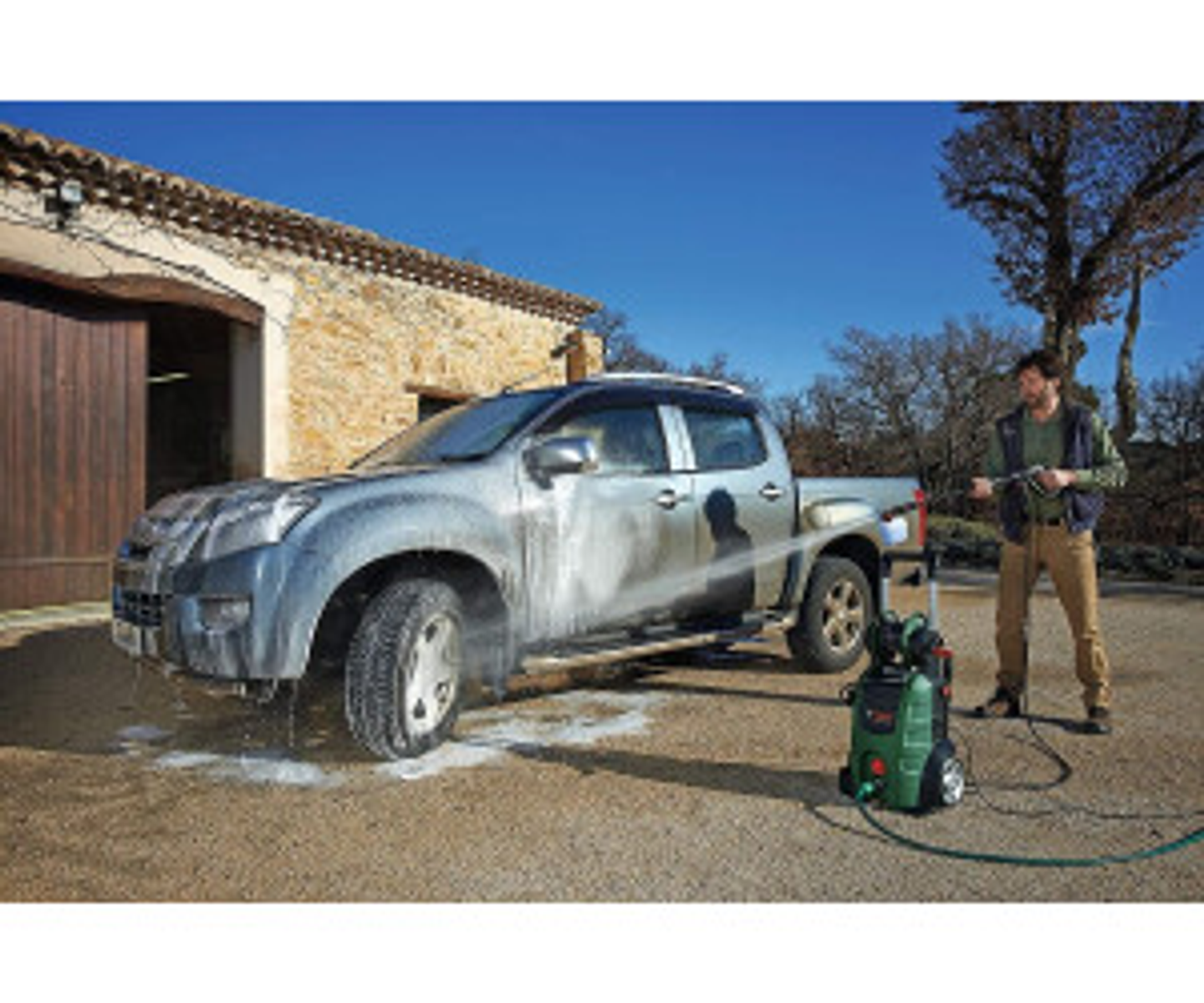 Uomo che lava un pick-up argentato con un'idropulitrice in una giornata di sole.
