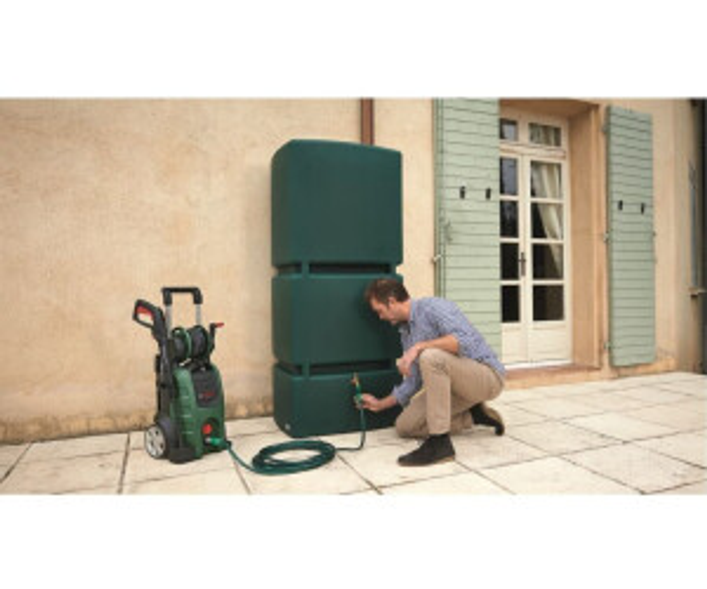 Un uomo collega un tubo a un serbatoio d'acqua verde vicino a un'idropulitrice. All'aperto.