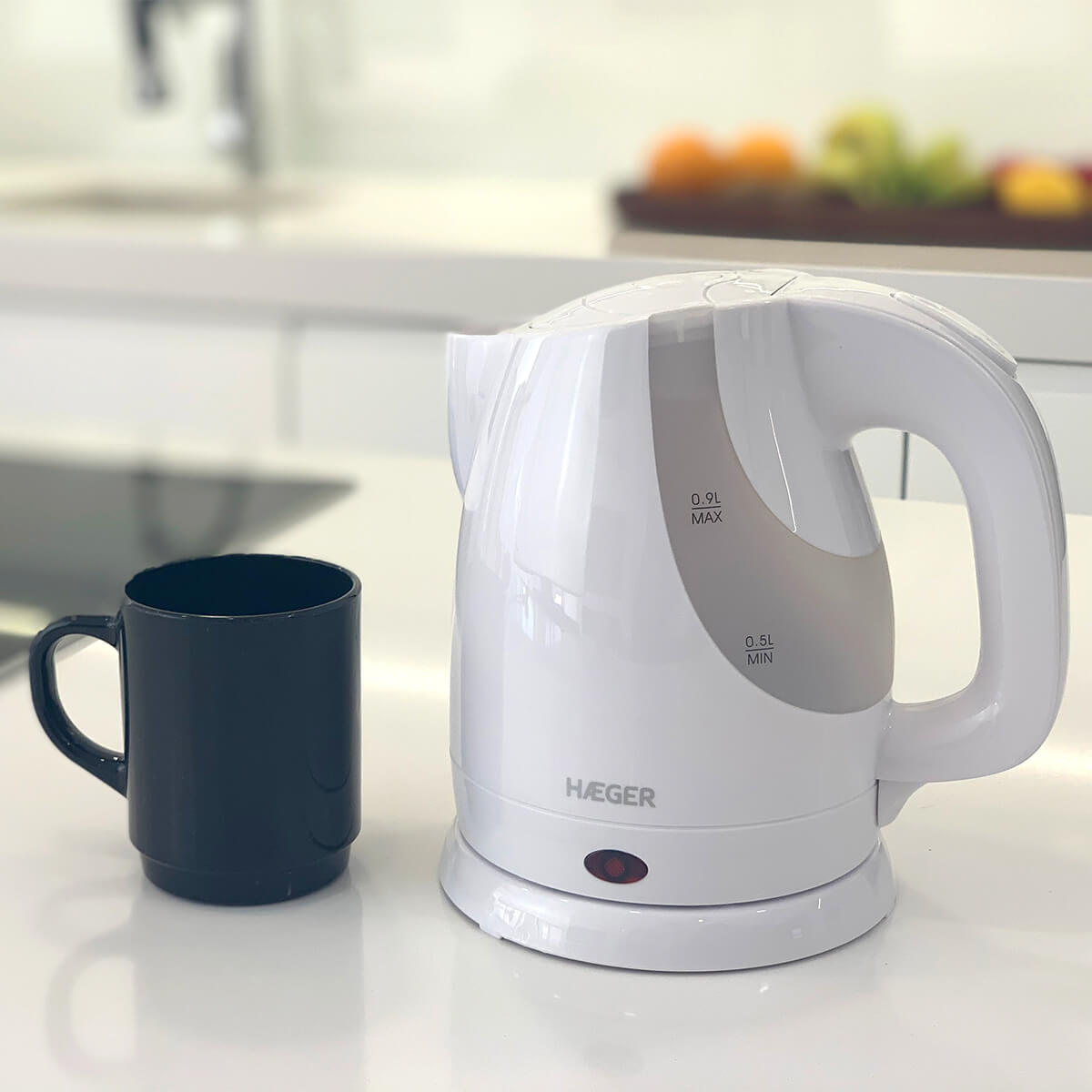 Bollitore elettrico bianco e tazza nera su un bancone bianco. Sfondo cucina.