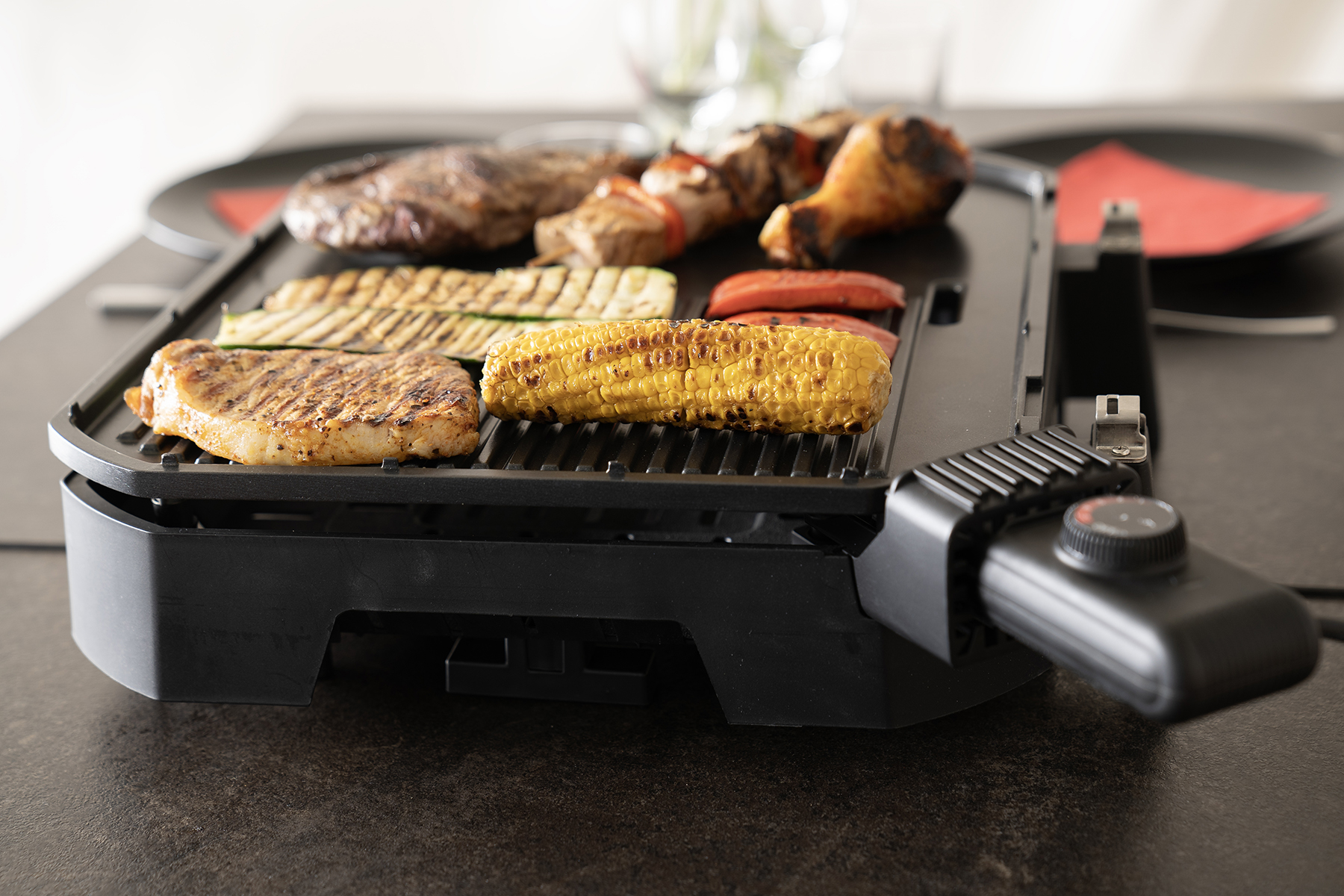 Grill mit verschiedenen Speisen: Steak, Mais, Würstchen und Gemüse. Schwarzer Tisch.