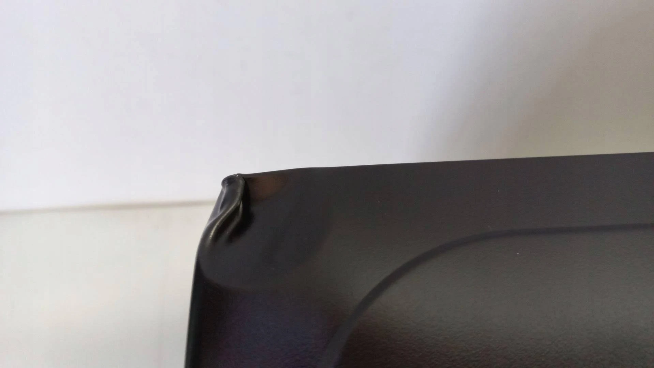 Zbliżenie rogu czarnego przedmiotu z niewielkim wgnieceniem.