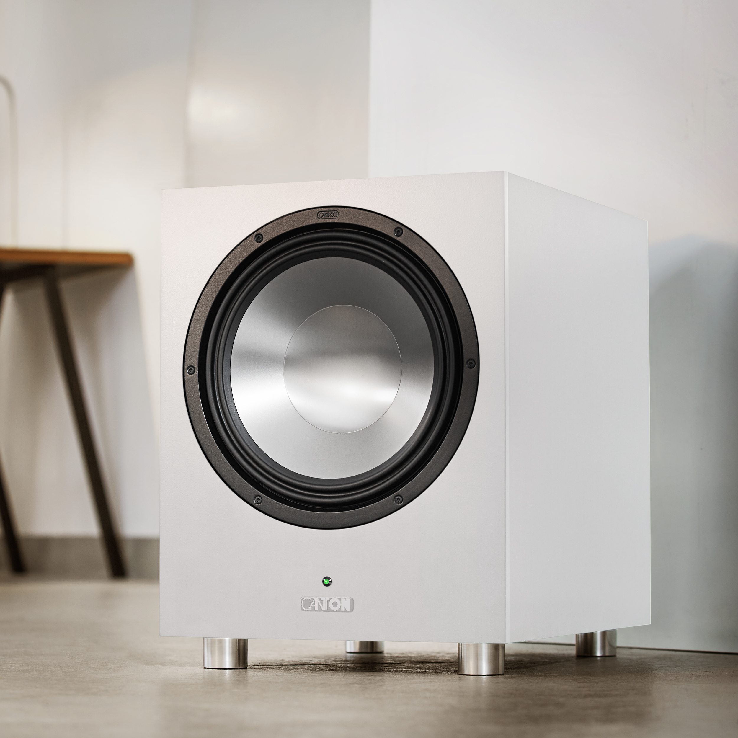Weißer Subwoofer-Lautsprecher. Schwarzer Lautsprecher und Zierleiste. Silberne Beine. Weiße Wand.