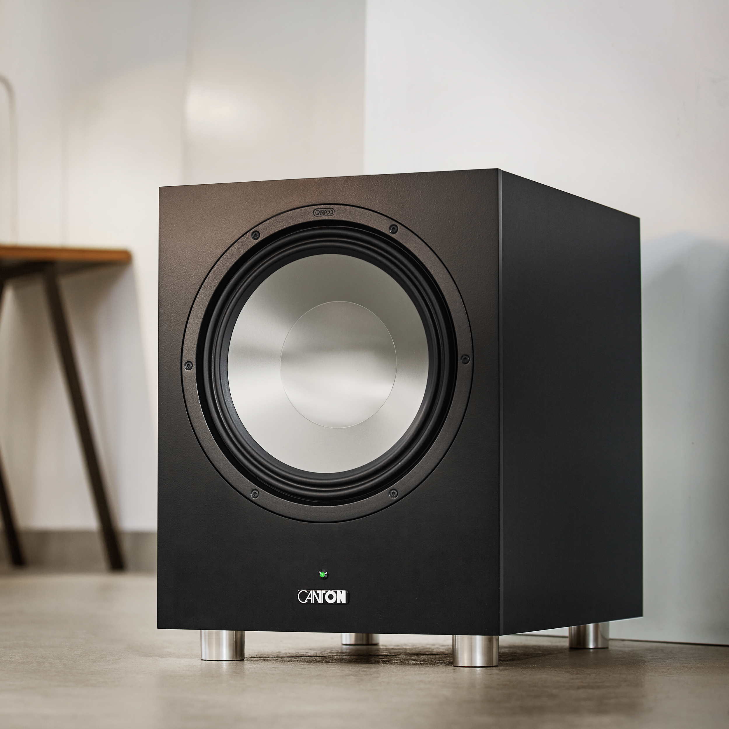 Ein schwarzer Subwoofer mit einem silbernen Lautsprecher, platziert auf einem Holzboden.