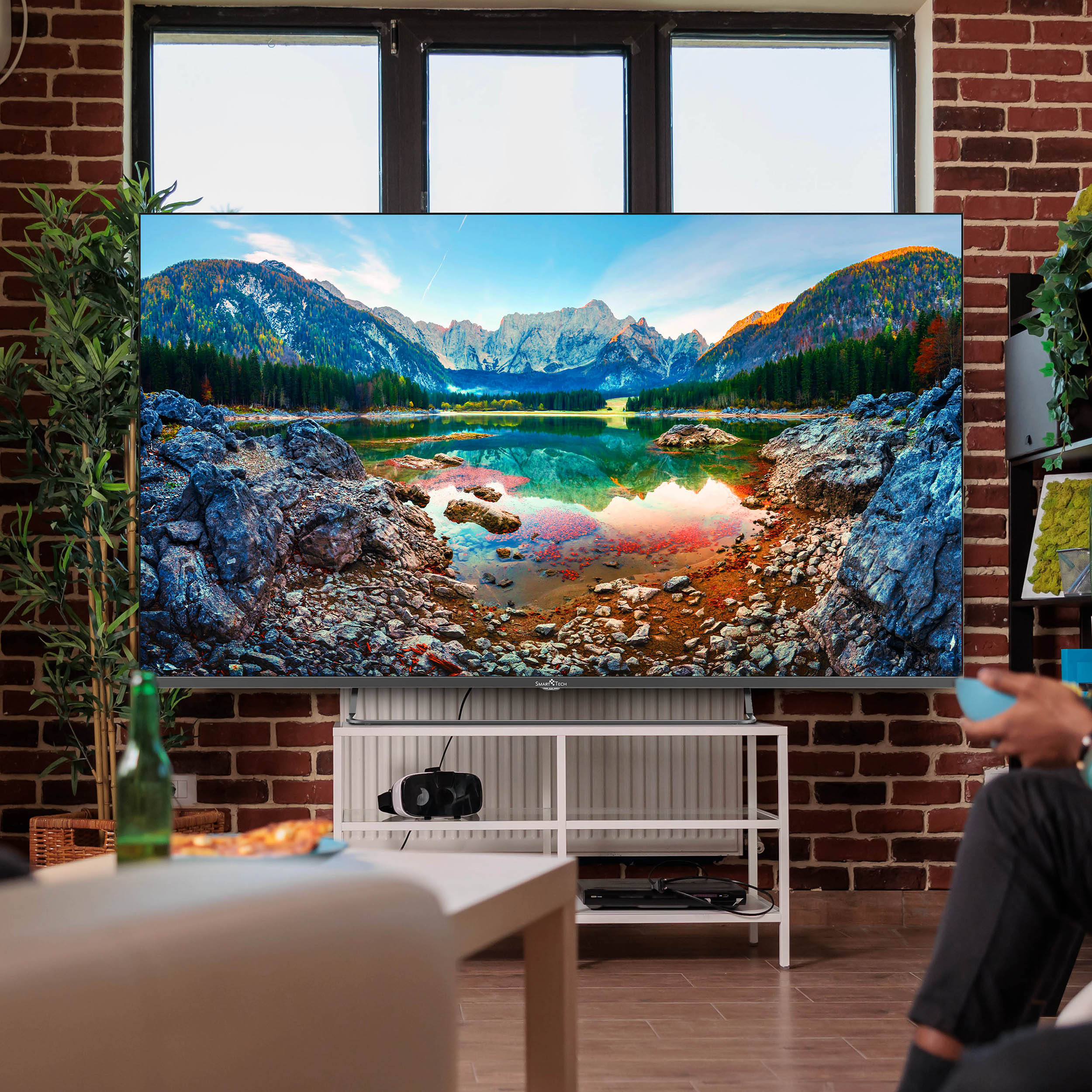 Salon z dużym telewizorem, pokazującym krajobraz. Osoba na pierwszym planie.
