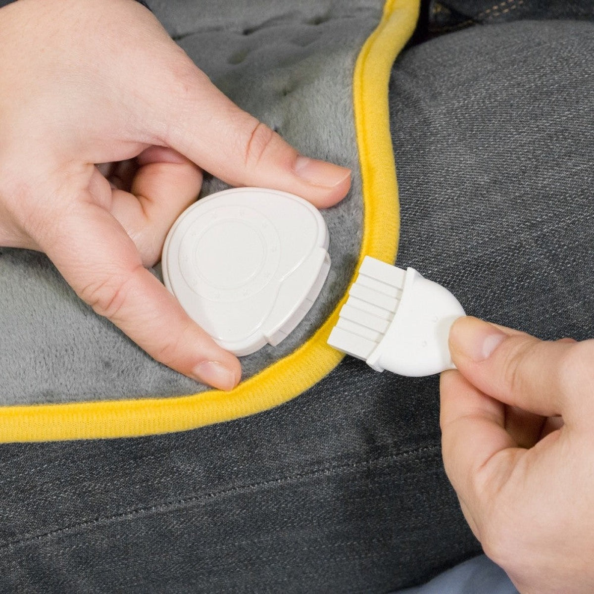 Dłonie z białym złączem i główką szczoteczki na szarej i żółtej powierzchni.