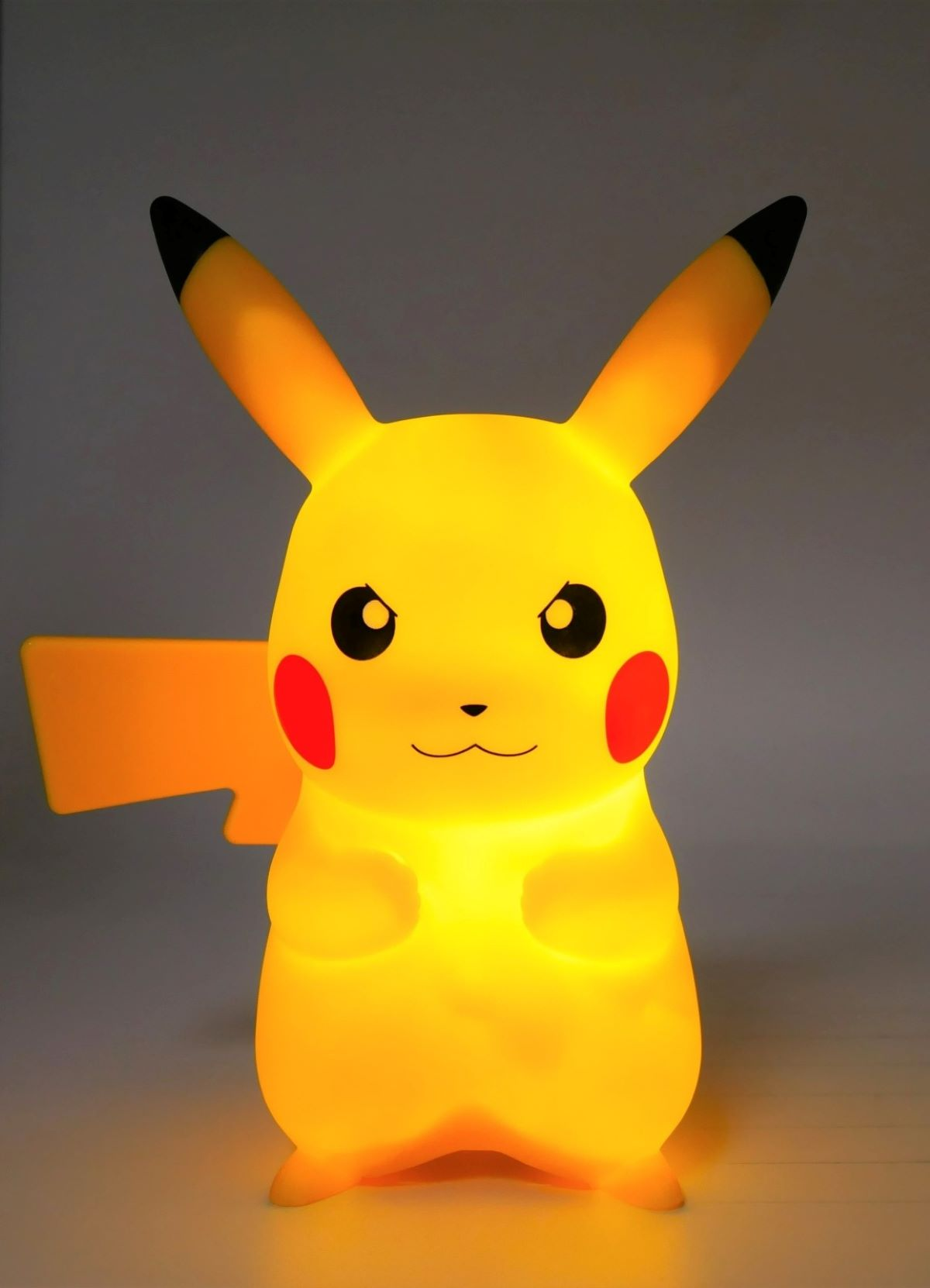 Una lámpara Pikachu amarilla está encendida. Tiene ojos negros y mejillas rojas. El fondo es blanco.